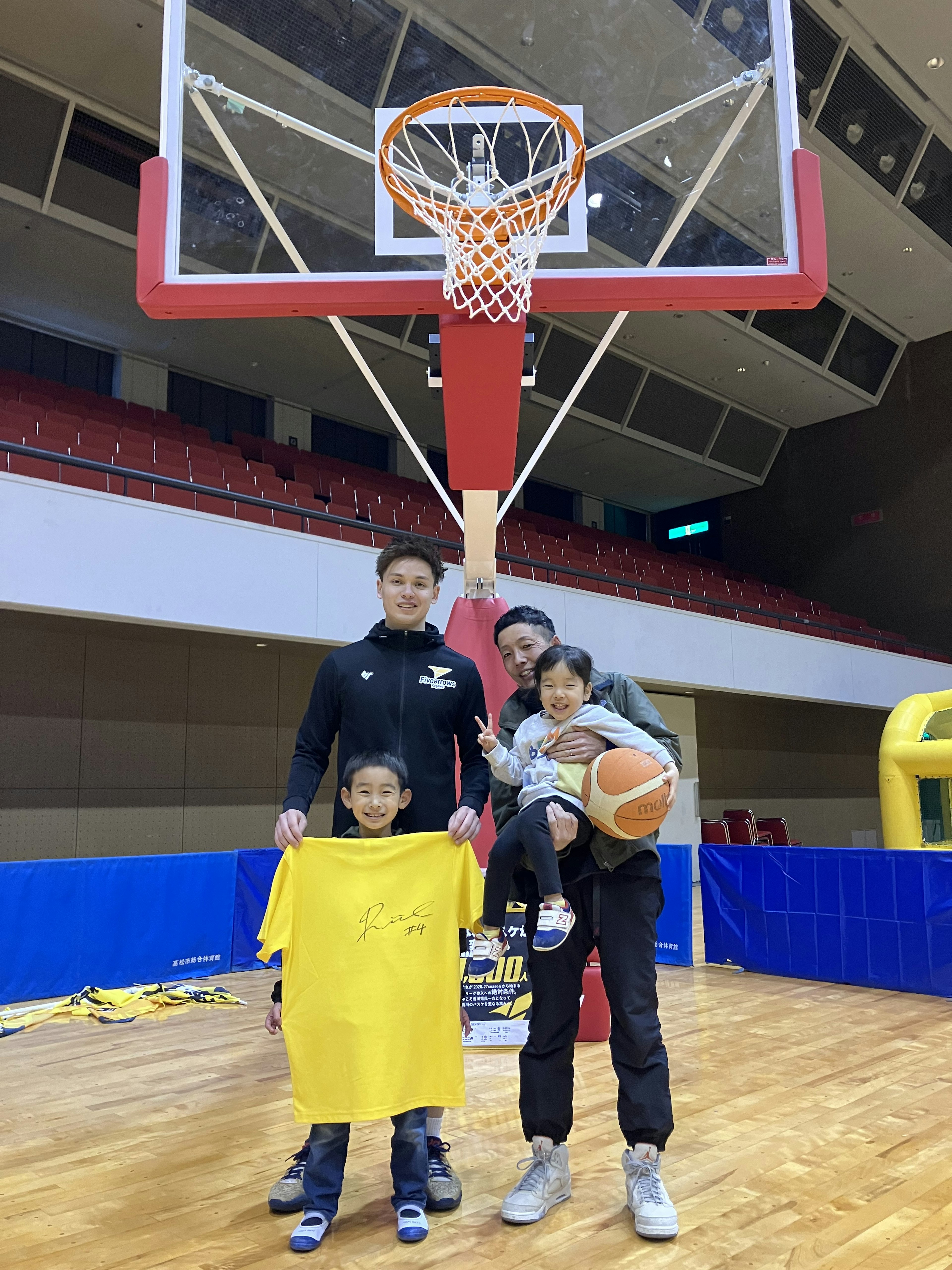 Un adulte posant avec des enfants sur un terrain de basket tenant un ballon de basket