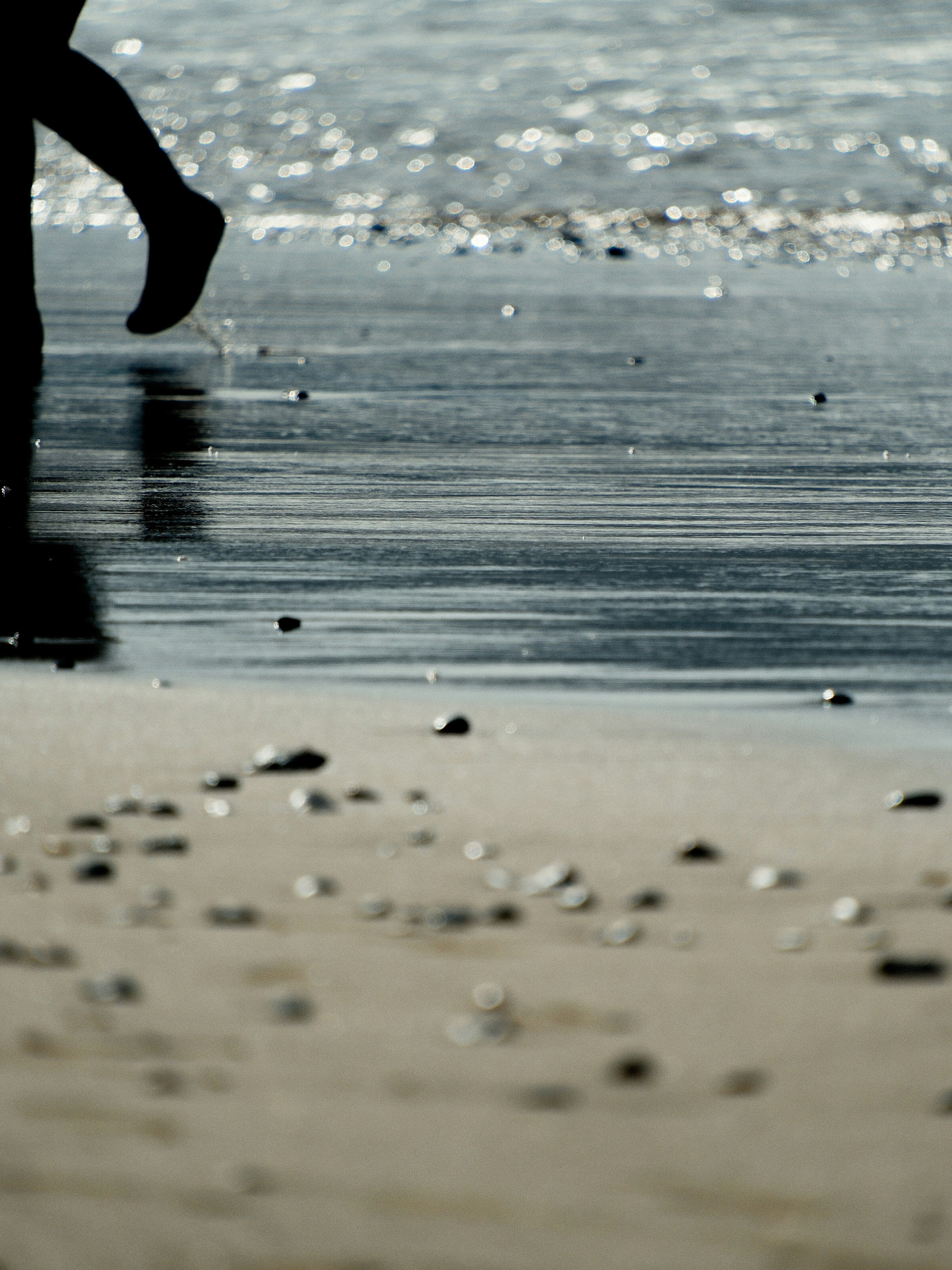 Person geht am Strand entlang mit Kieseln und nassem Sand