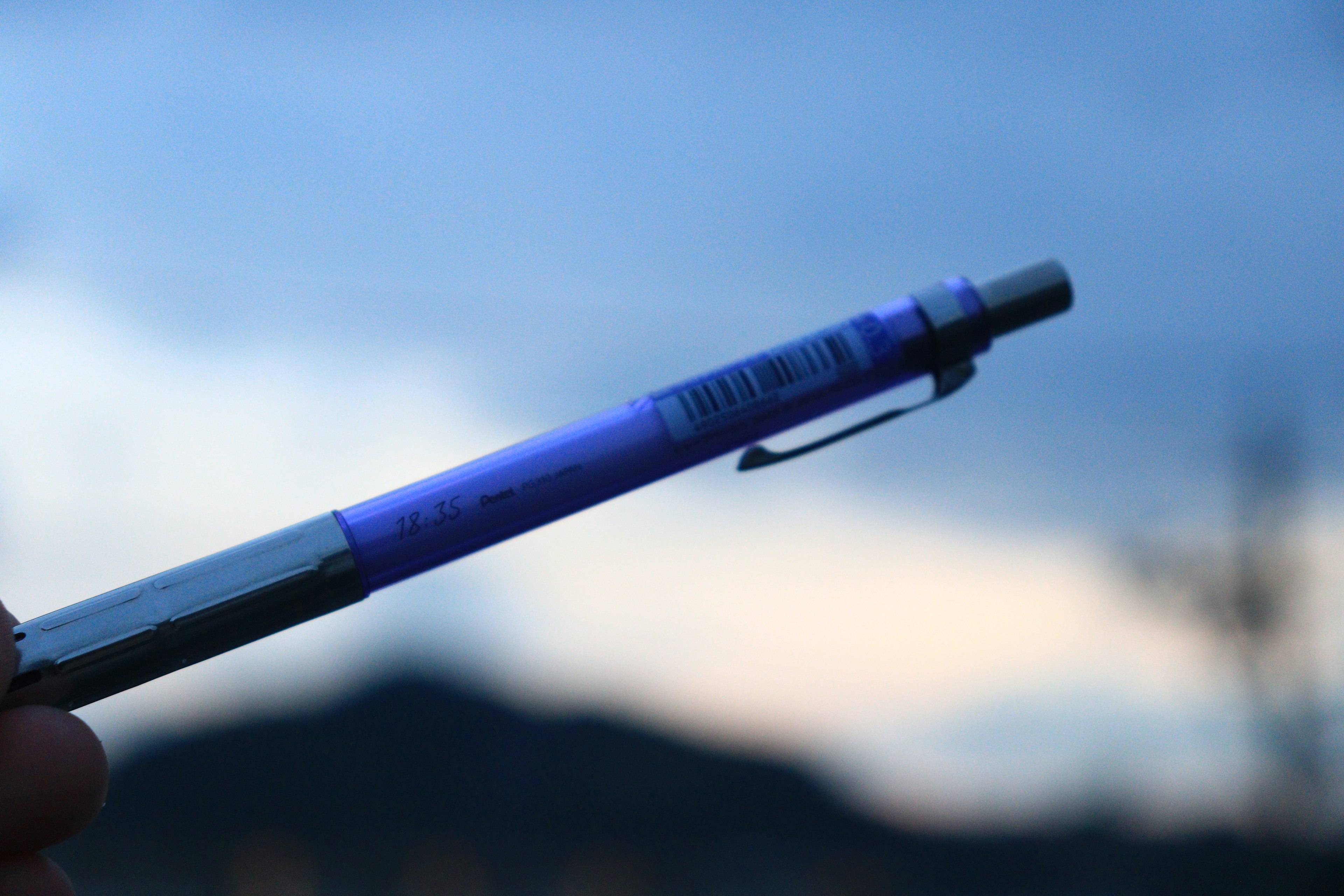 A purple pen held in hand against a beautiful landscape background