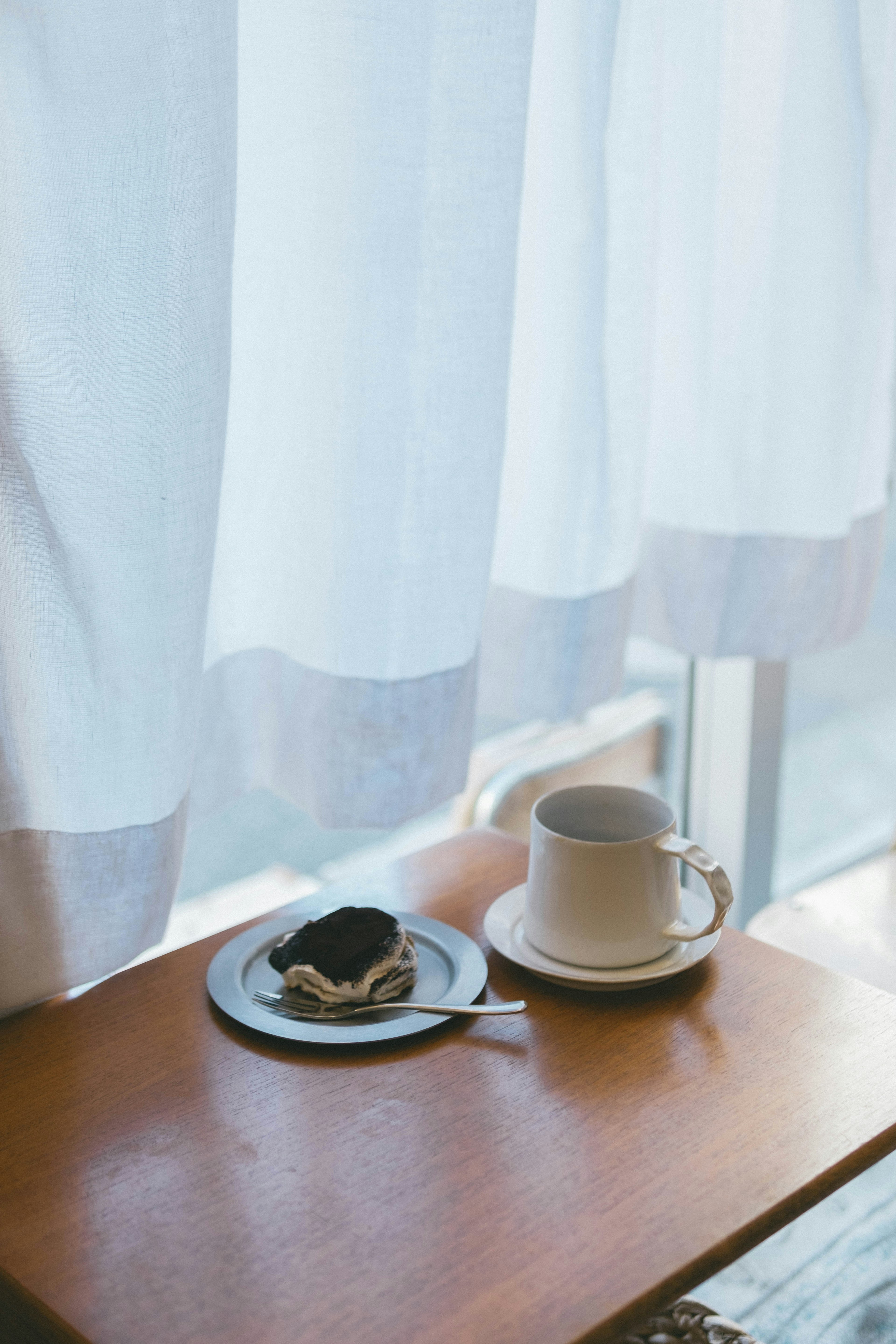 Taza de café y plato de postre visibles a través de cortinas blancas