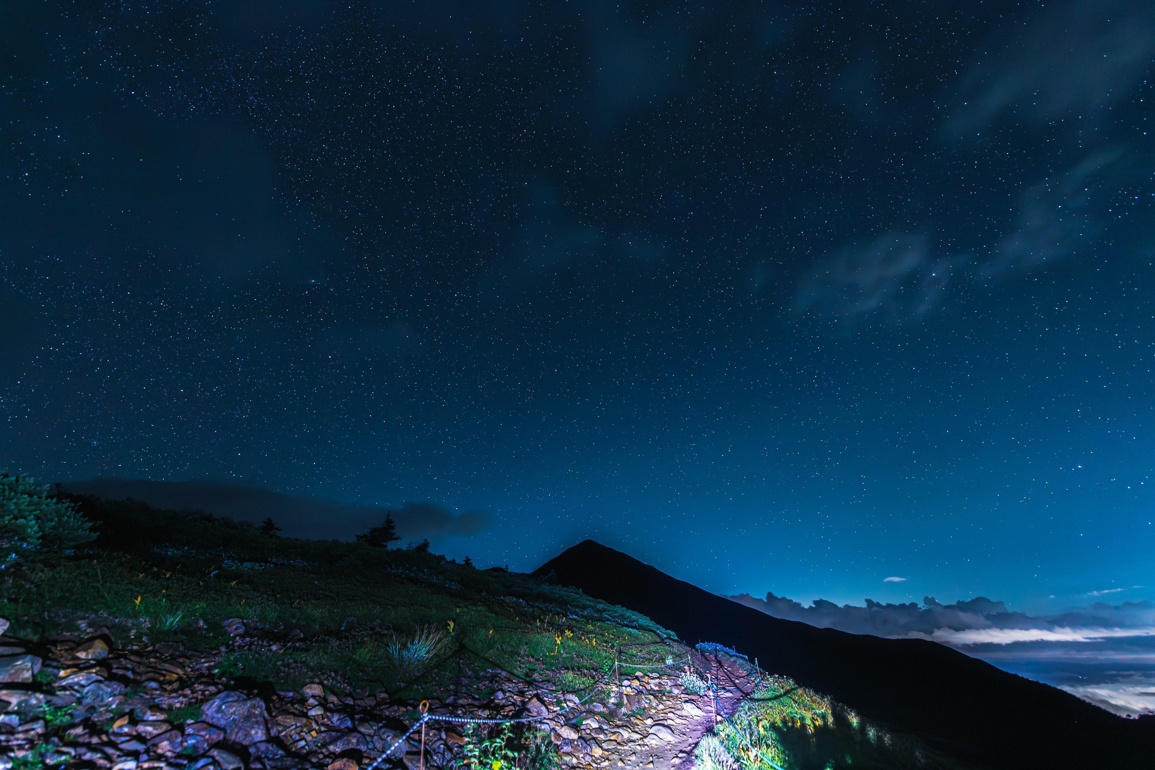 Nachtszene mit sternenklarem Himmel über einer Berglandschaft und beleuchtetem Pfad