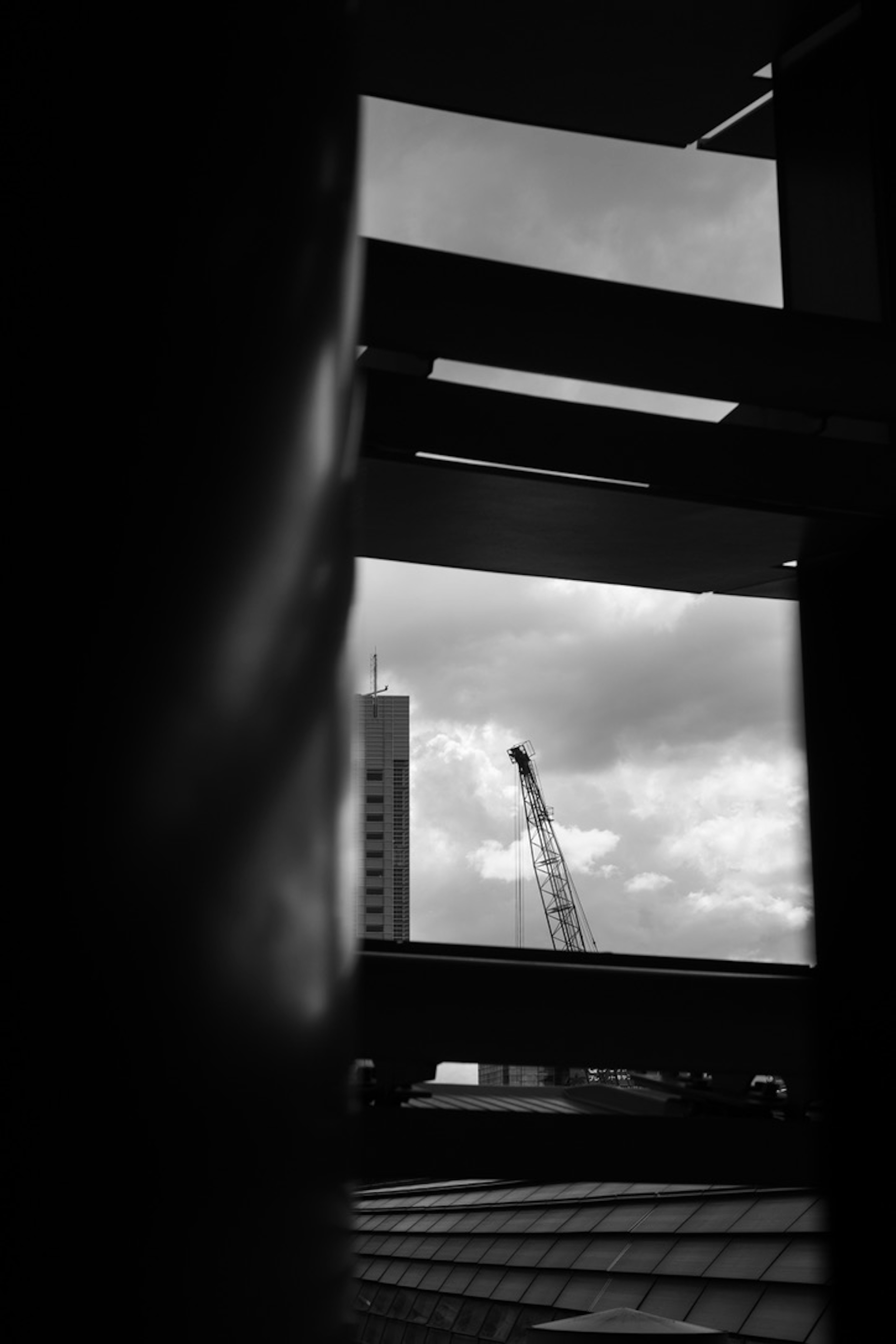 Image en noir et blanc montrant une grue de construction encadrée par des poutres structurelles