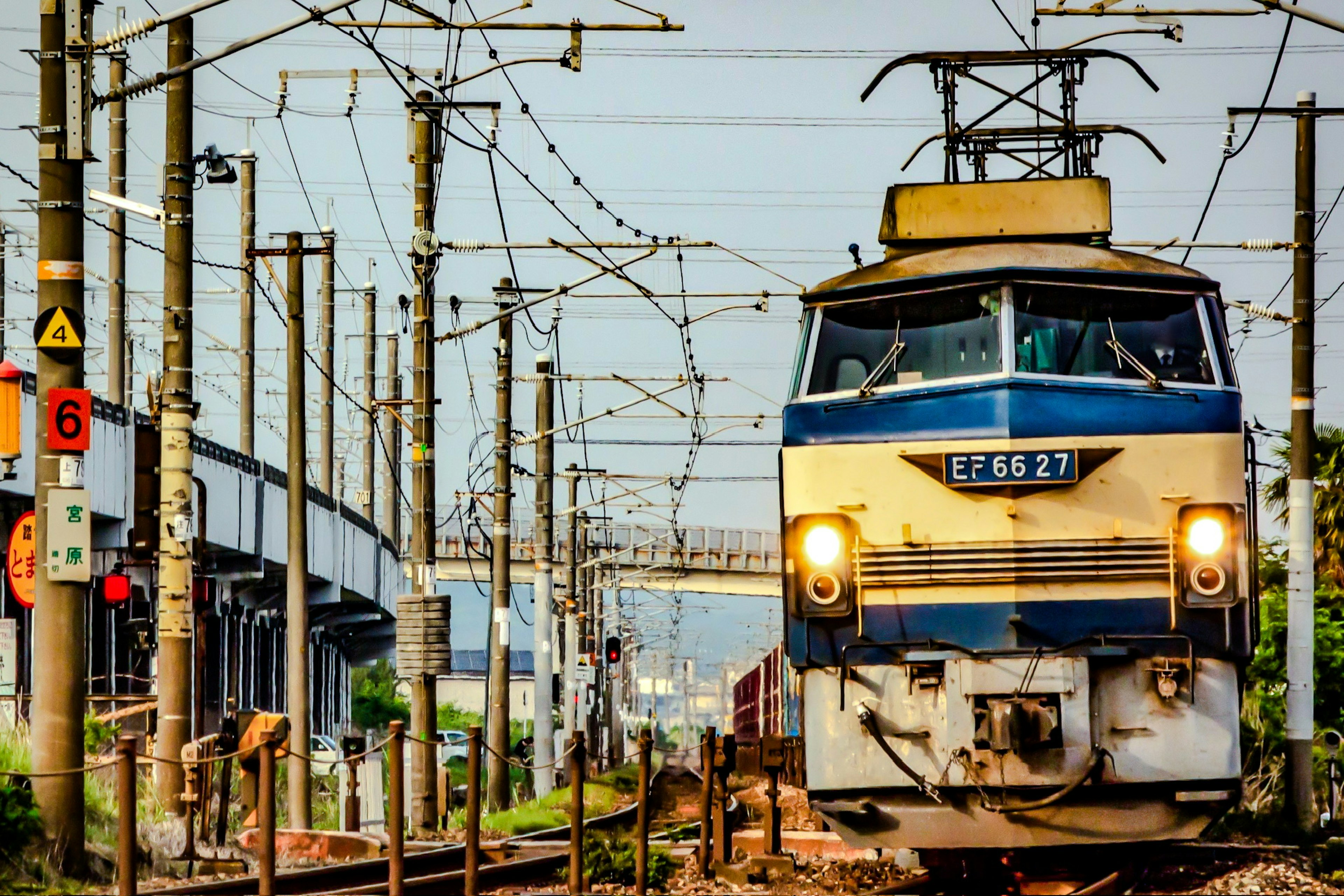 Un tren azul y blanco en las vías con cables aéreos de fondo