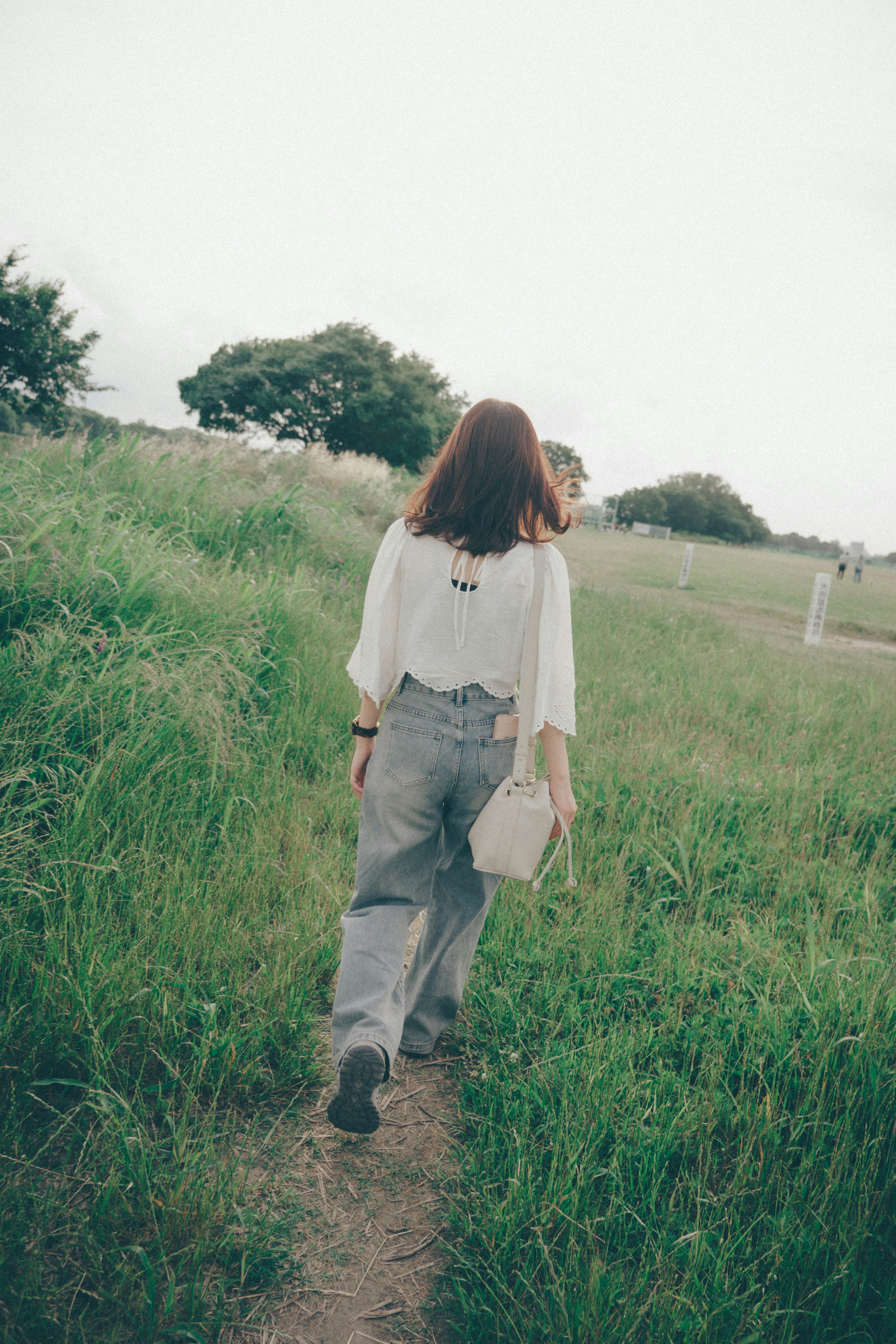 Una mujer caminando en un campo de hierba con una blusa blanca y jeans