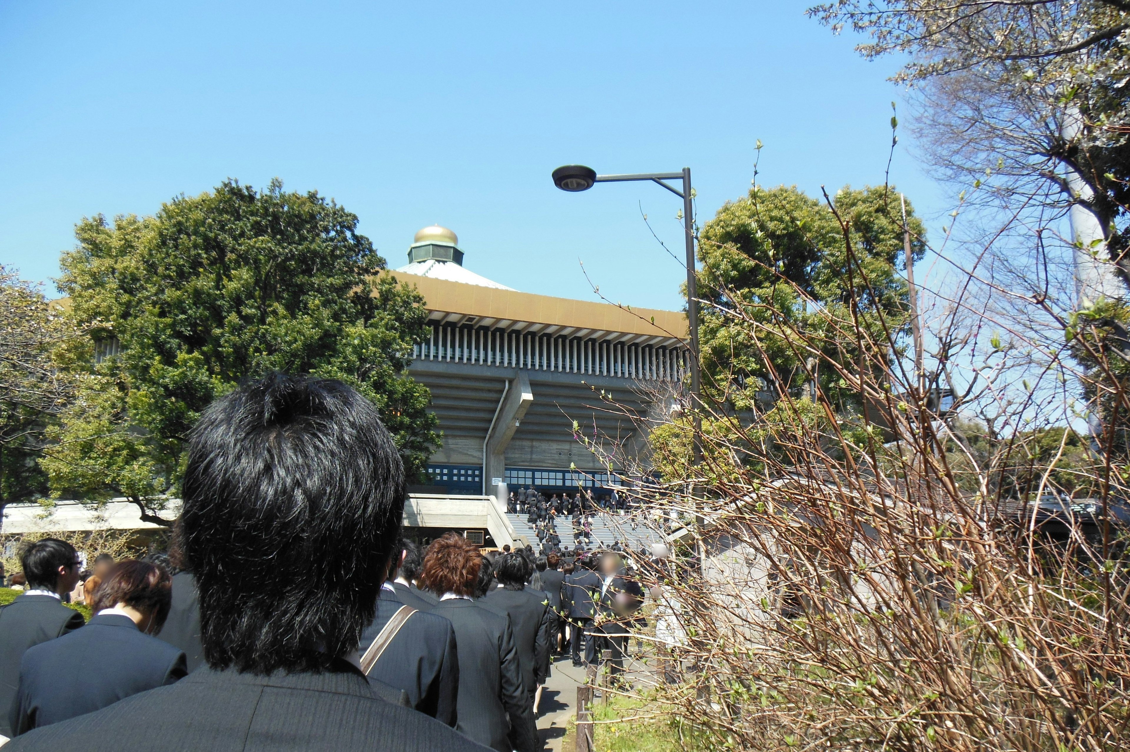 人々が集まる場所に向かう様子の写真で、背景には大きな建物と青空が広がっている