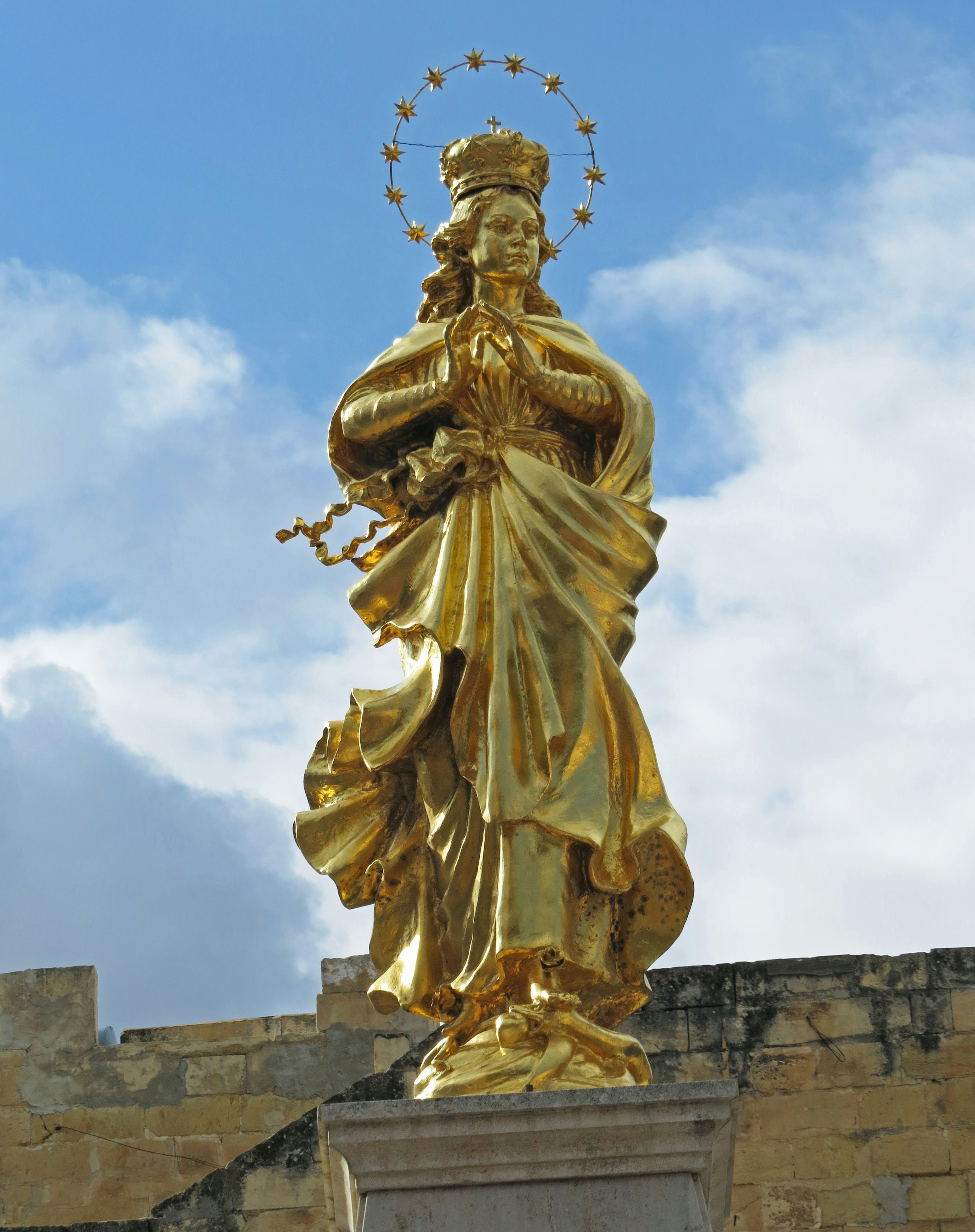 Golden statue of the Virgin Mary standing under a blue sky