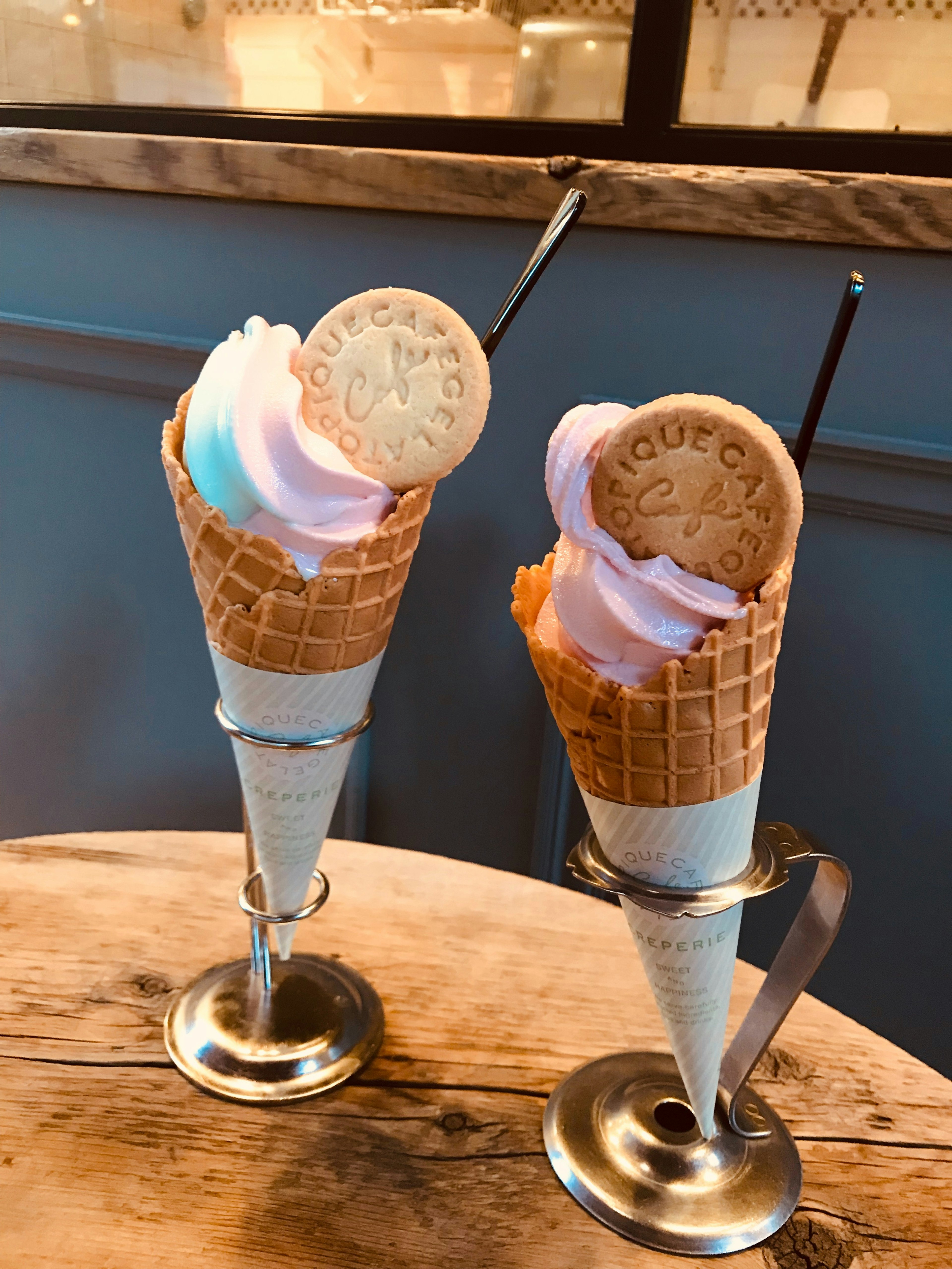 Dos conos de helado servidos en soportes de plata con espirales de colores pastel y galletas encima