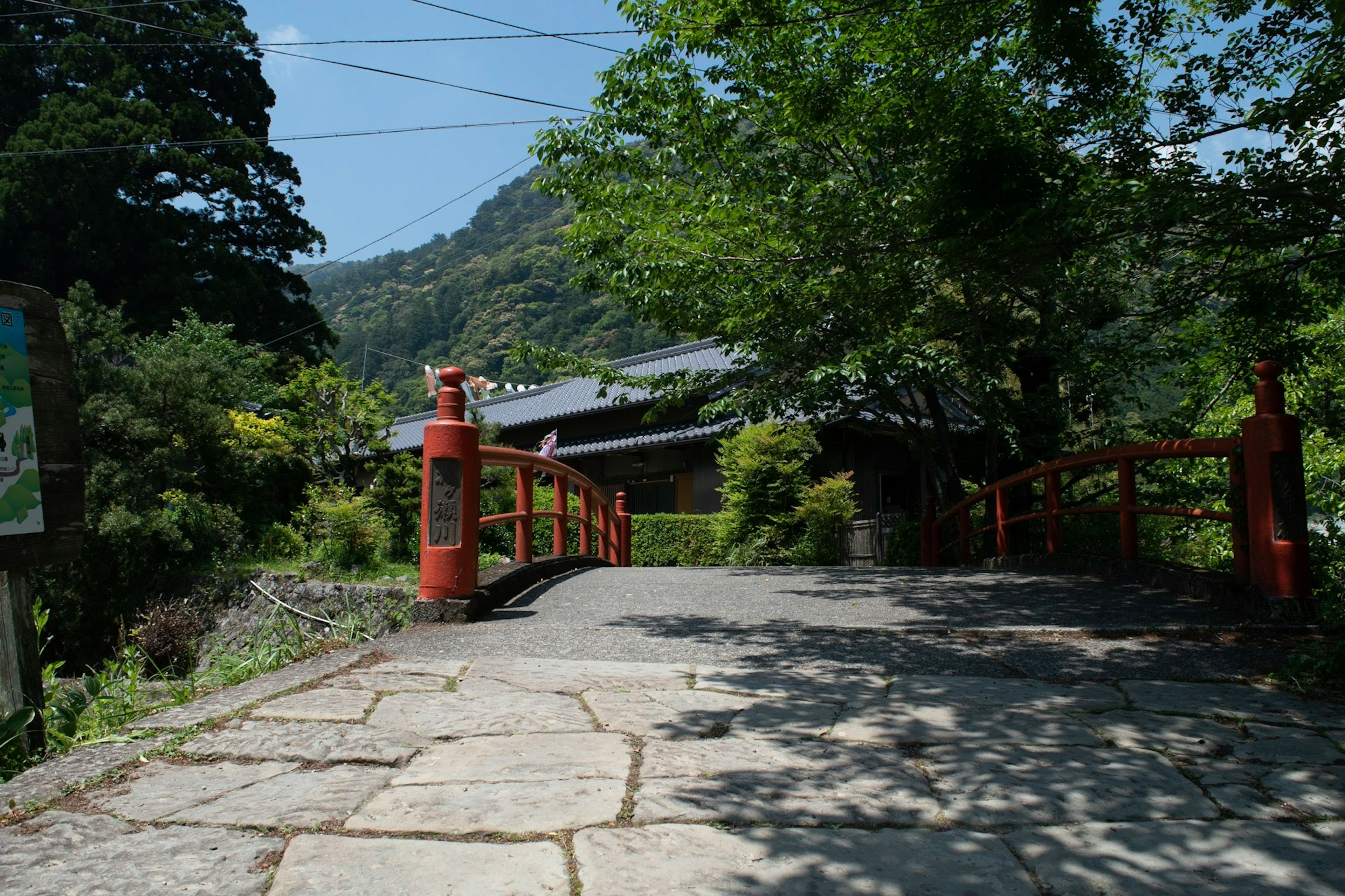 Maison japonaise traditionnelle entourée de nature avec un pont rouge