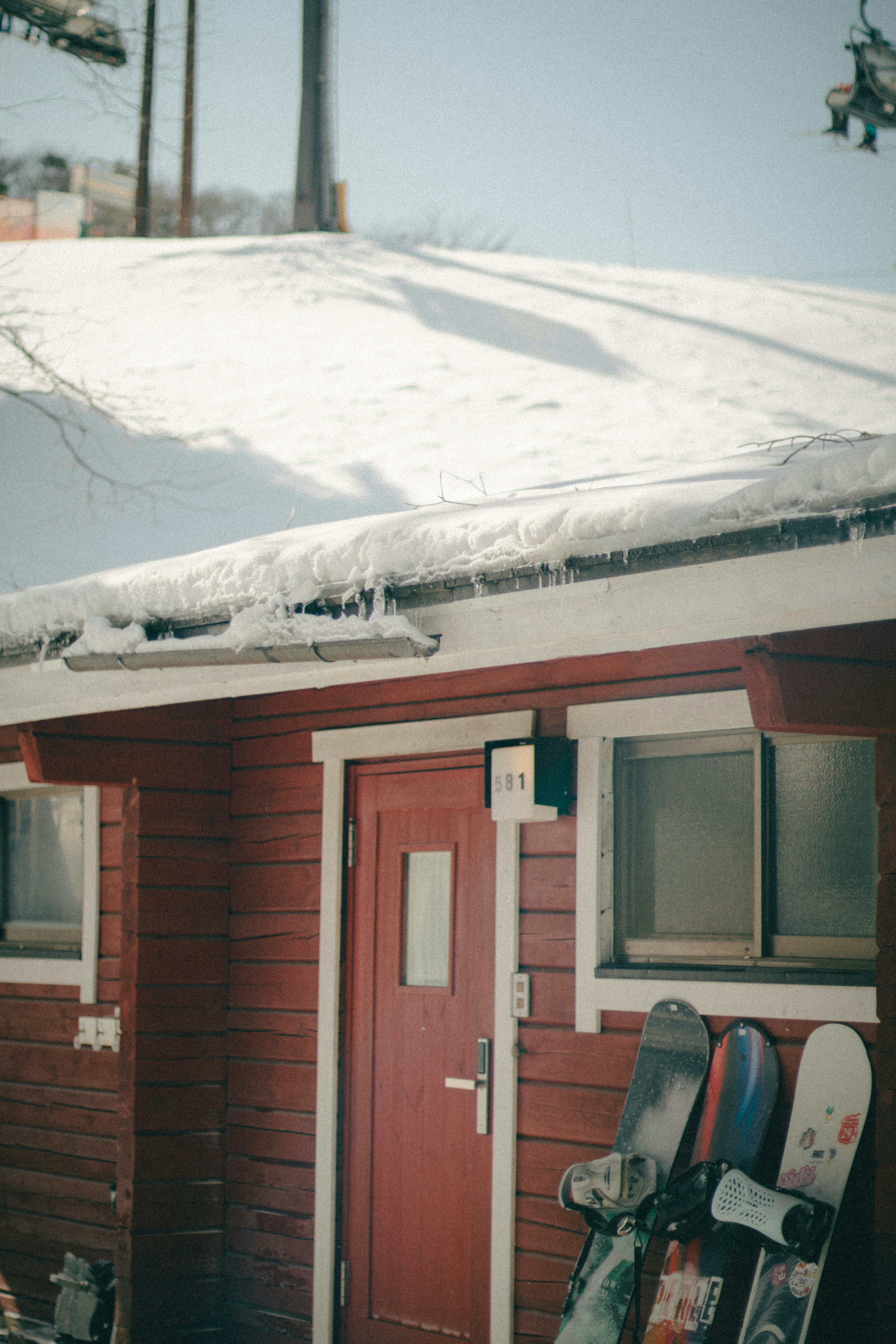 Red cabin with a snow-covered roof and snowboards leaning against it