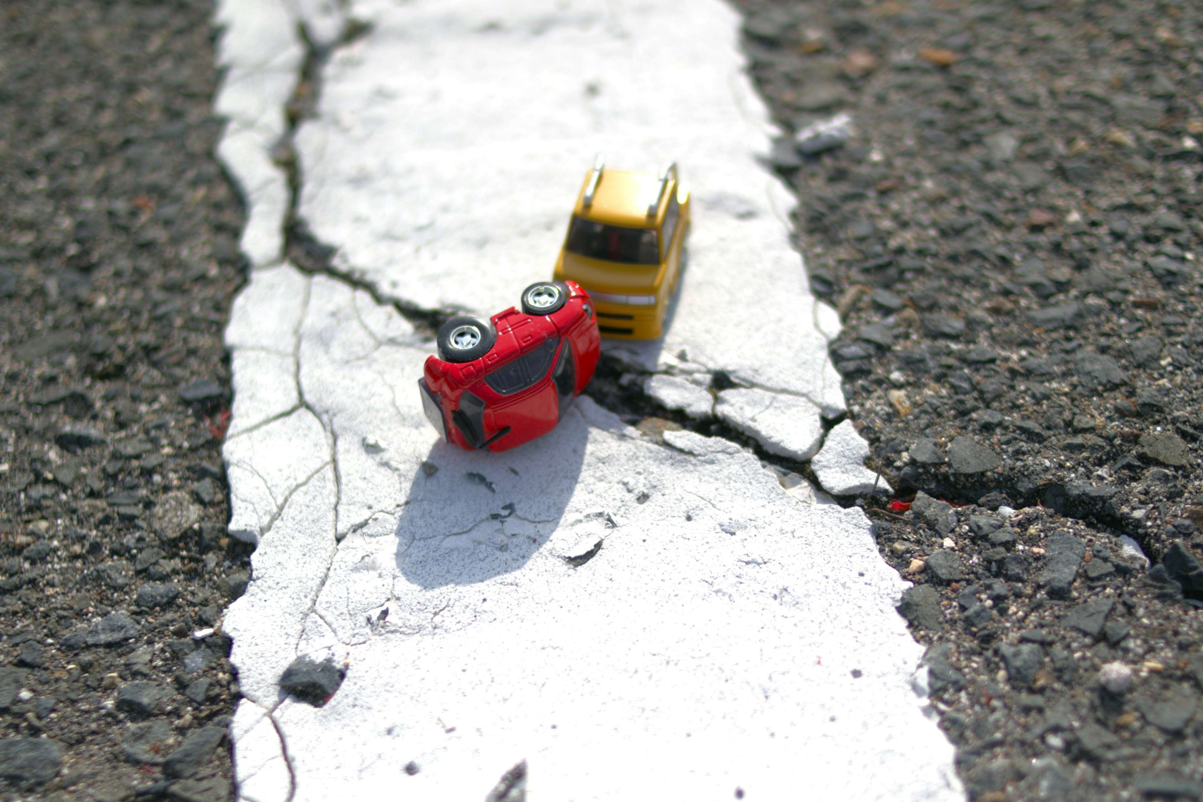 Un coche de juguete rojo y un coche de juguete amarillo están posicionados en una línea de carretera blanca agrietada