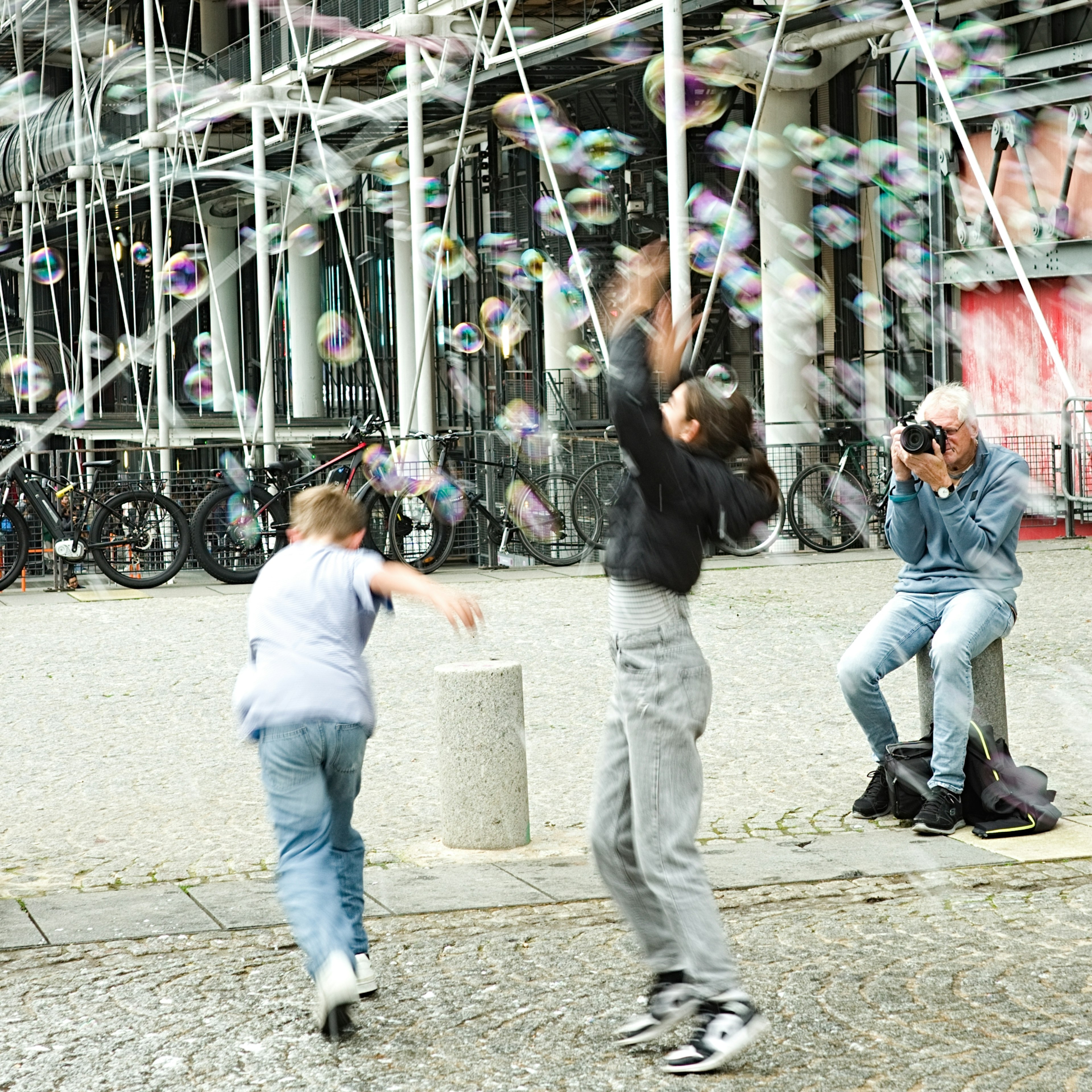 Children chasing bubbles while an adult photographs them in the background