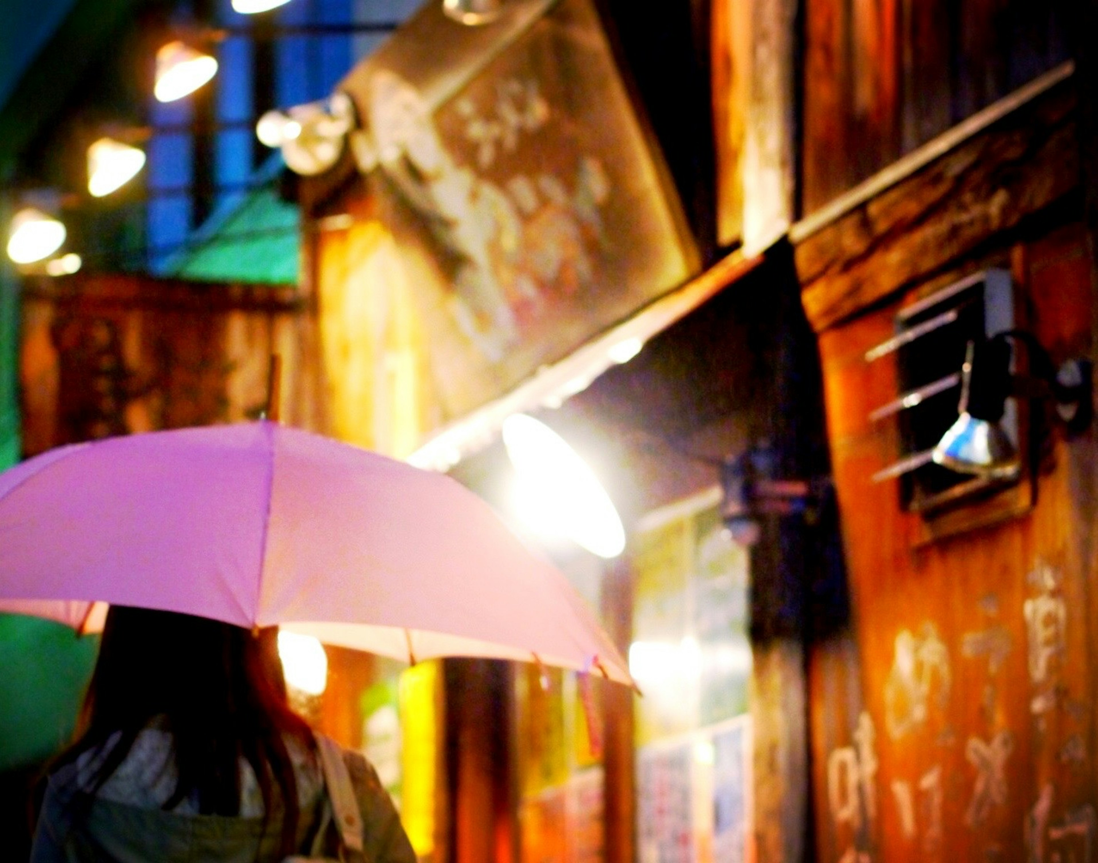 Une femme tenant un parapluie rose se tient devant un vieux bâtiment illuminé par des lumières colorées