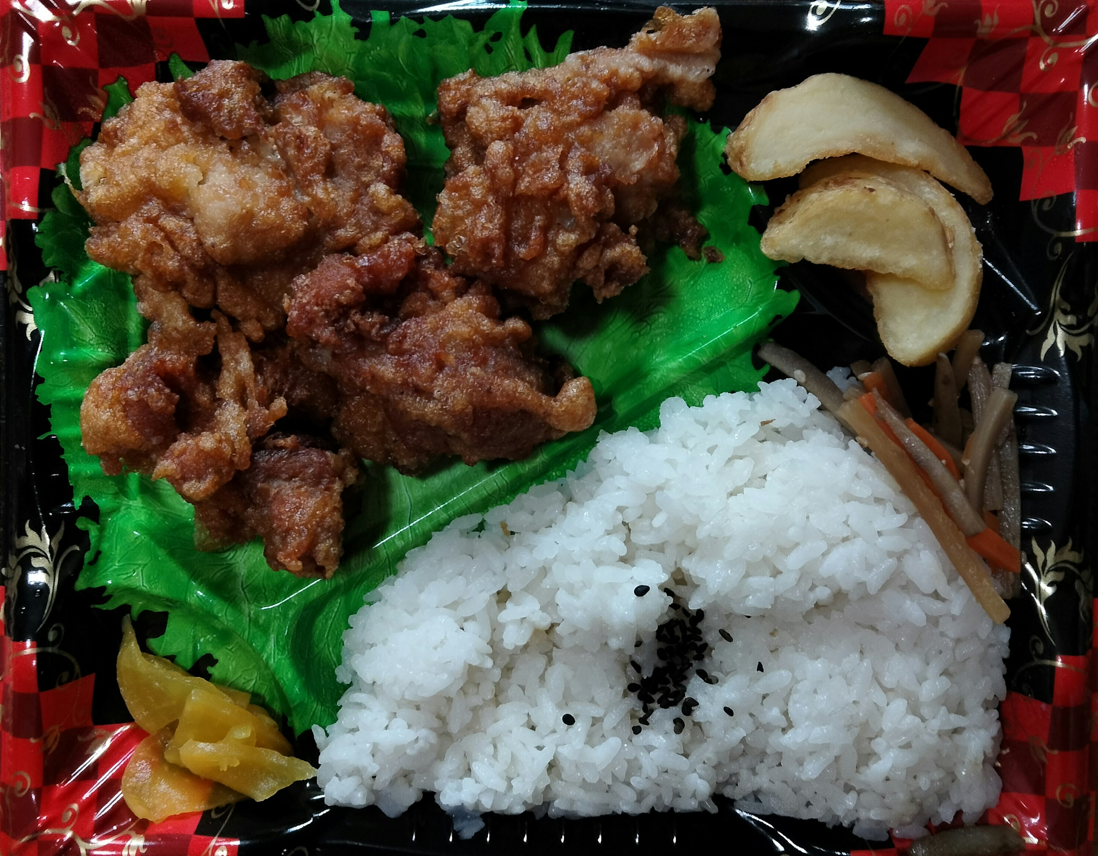 Bento box with fried chicken and rice arranged on green lettuce and side dishes