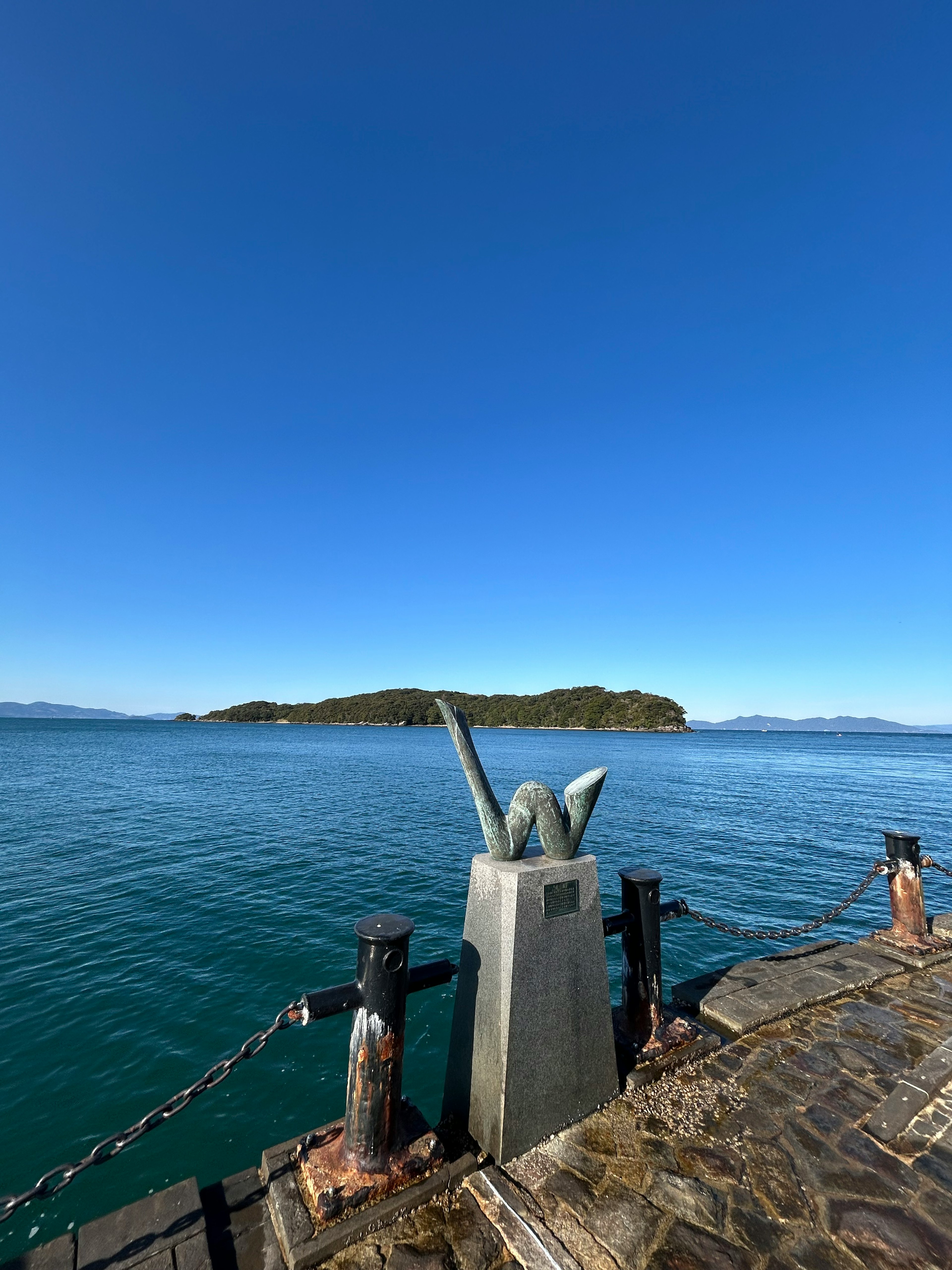 Sculpture at the end of a pier with a clear blue sky and calm sea