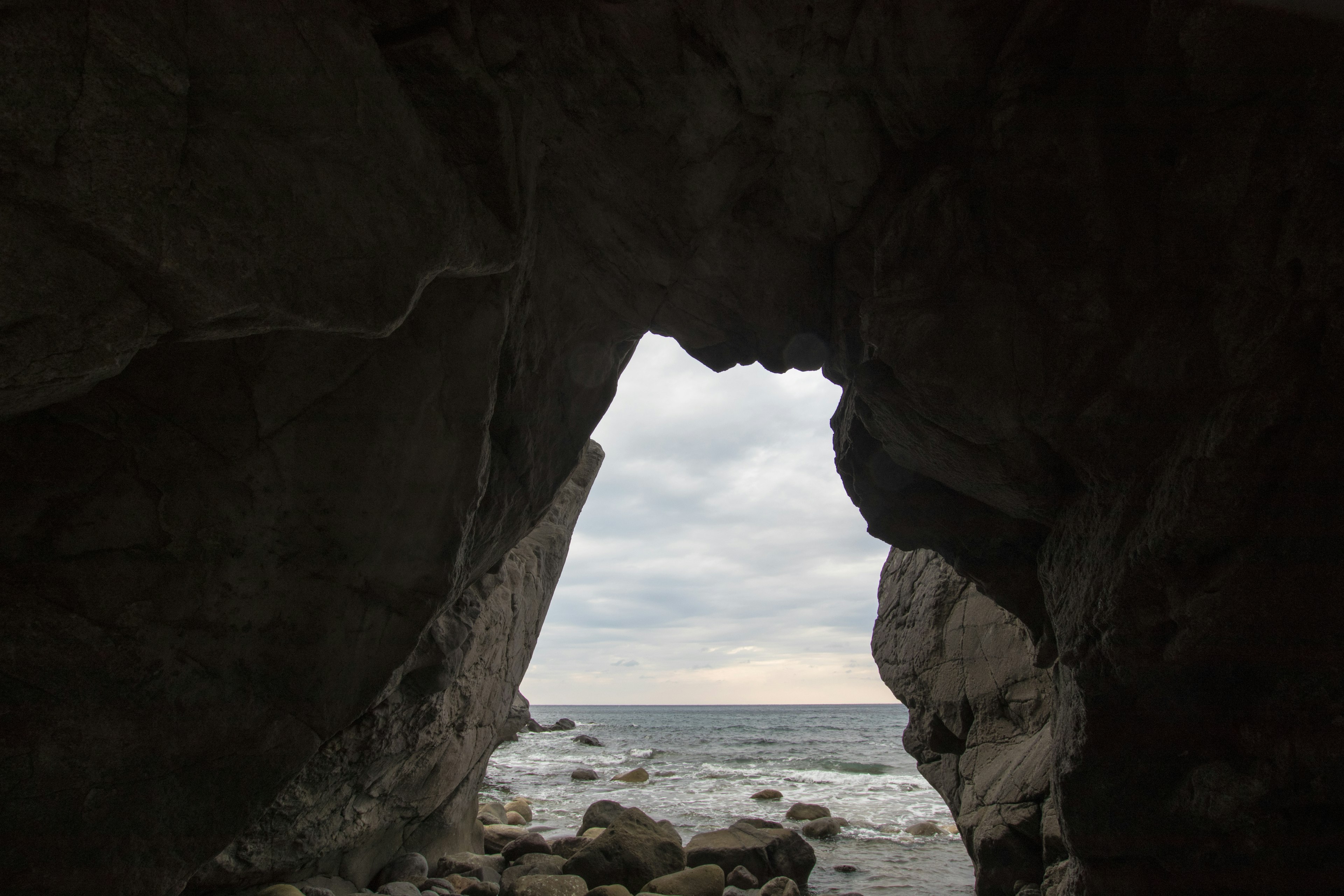 View of the ocean and cloudy sky through a rock tunnel