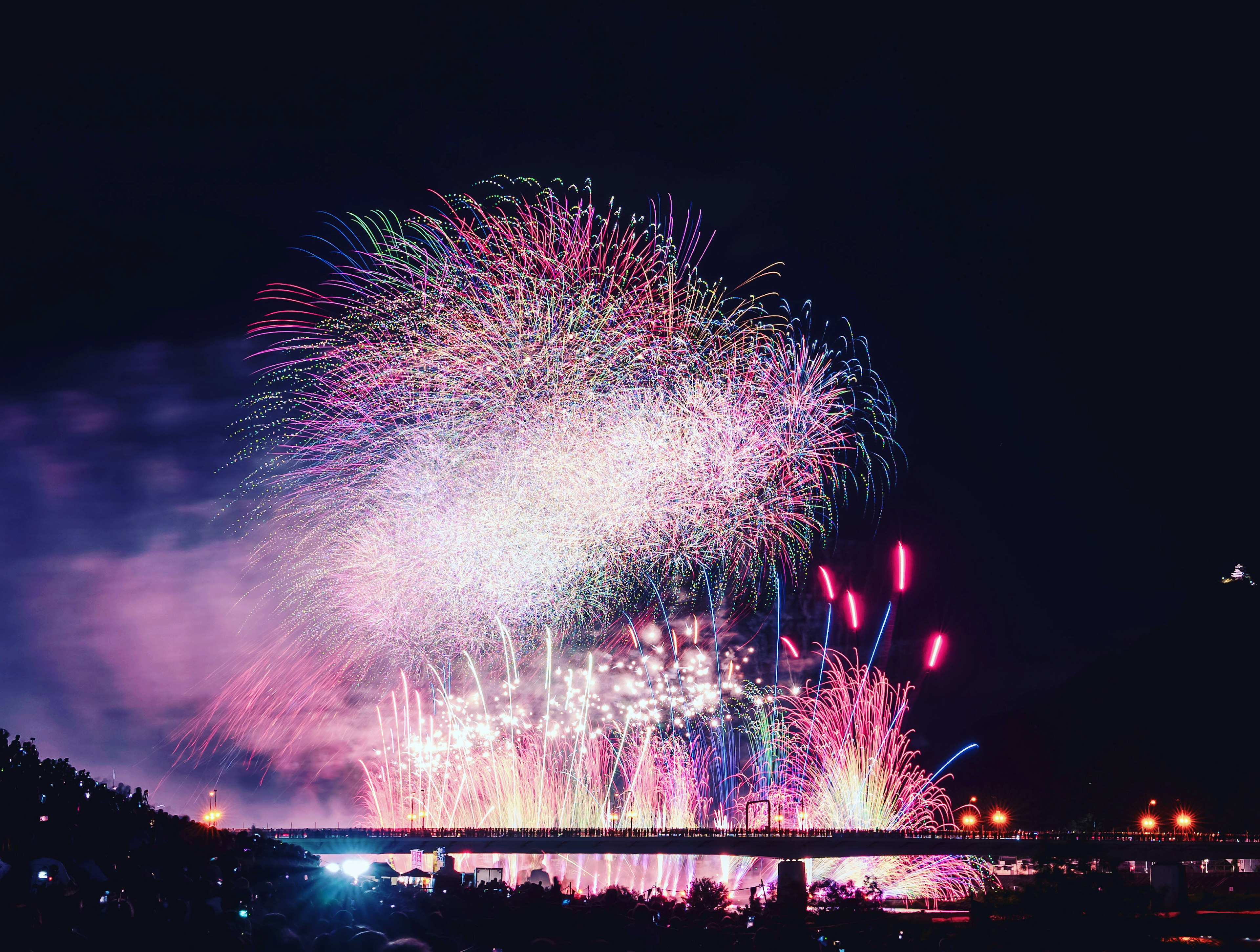 Colorful fireworks display in the night sky with a bridge