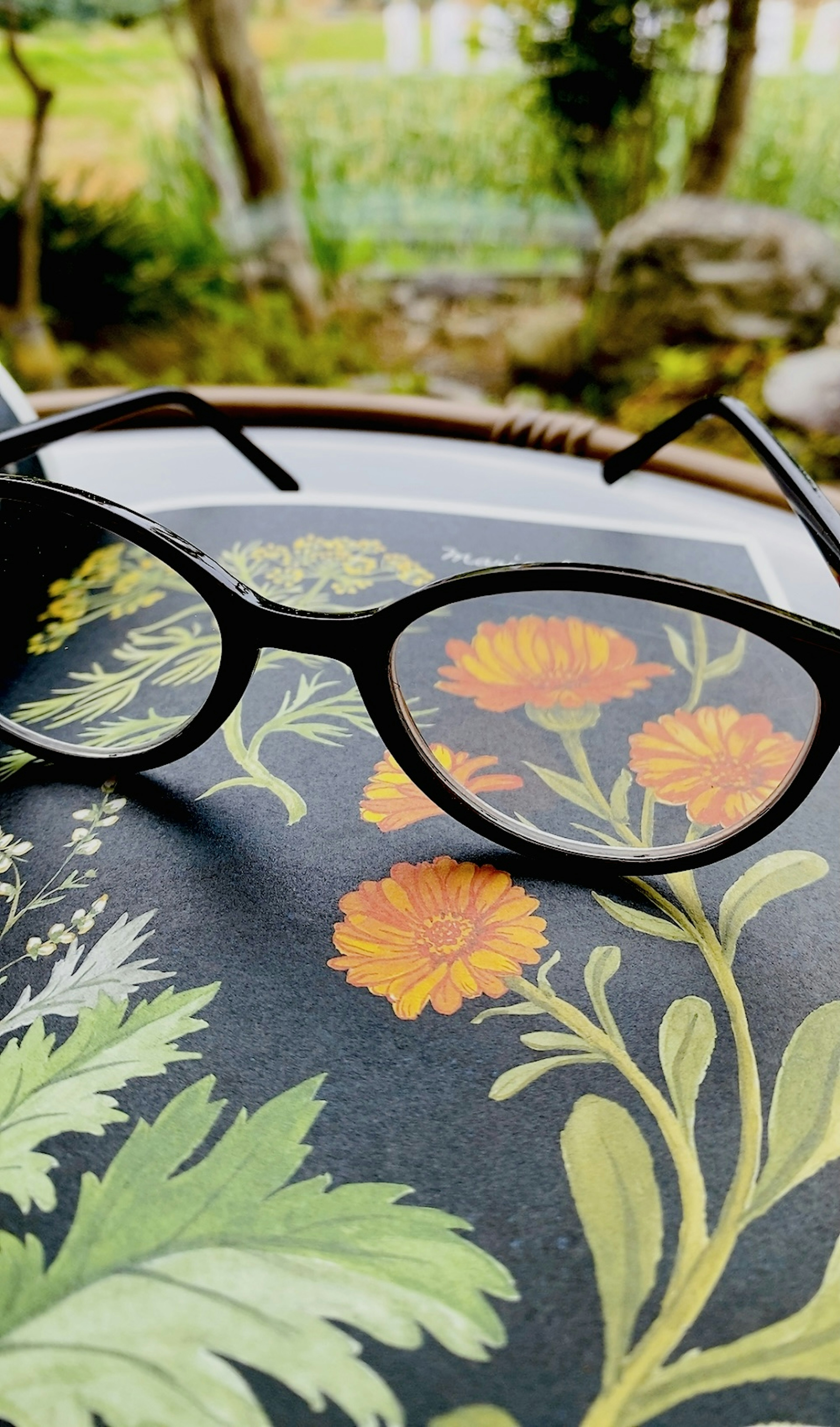 Black glasses resting on a floral book with a green natural background