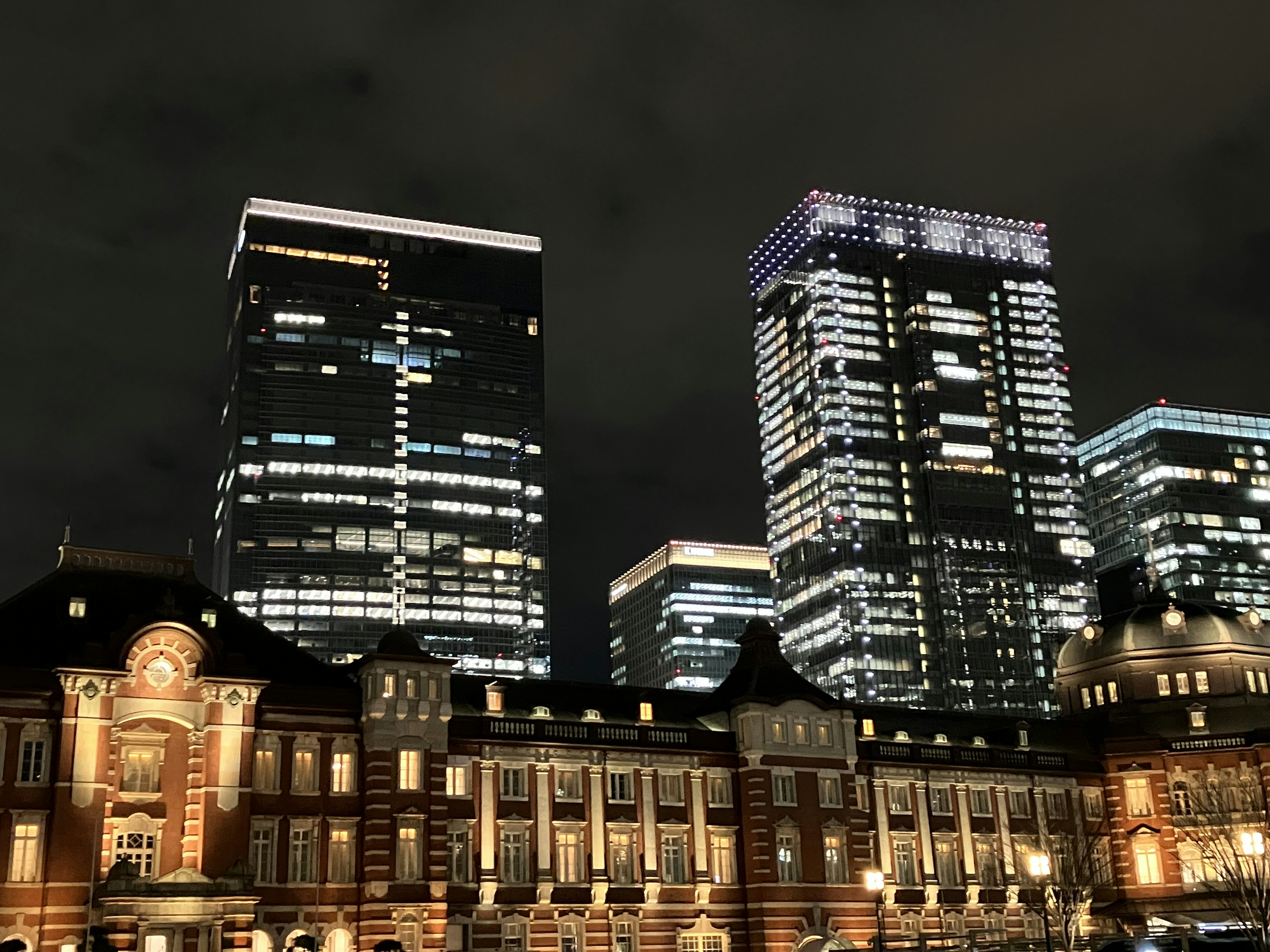 Vista nocturna de la estación de Tokio con rascacielos contrastantes