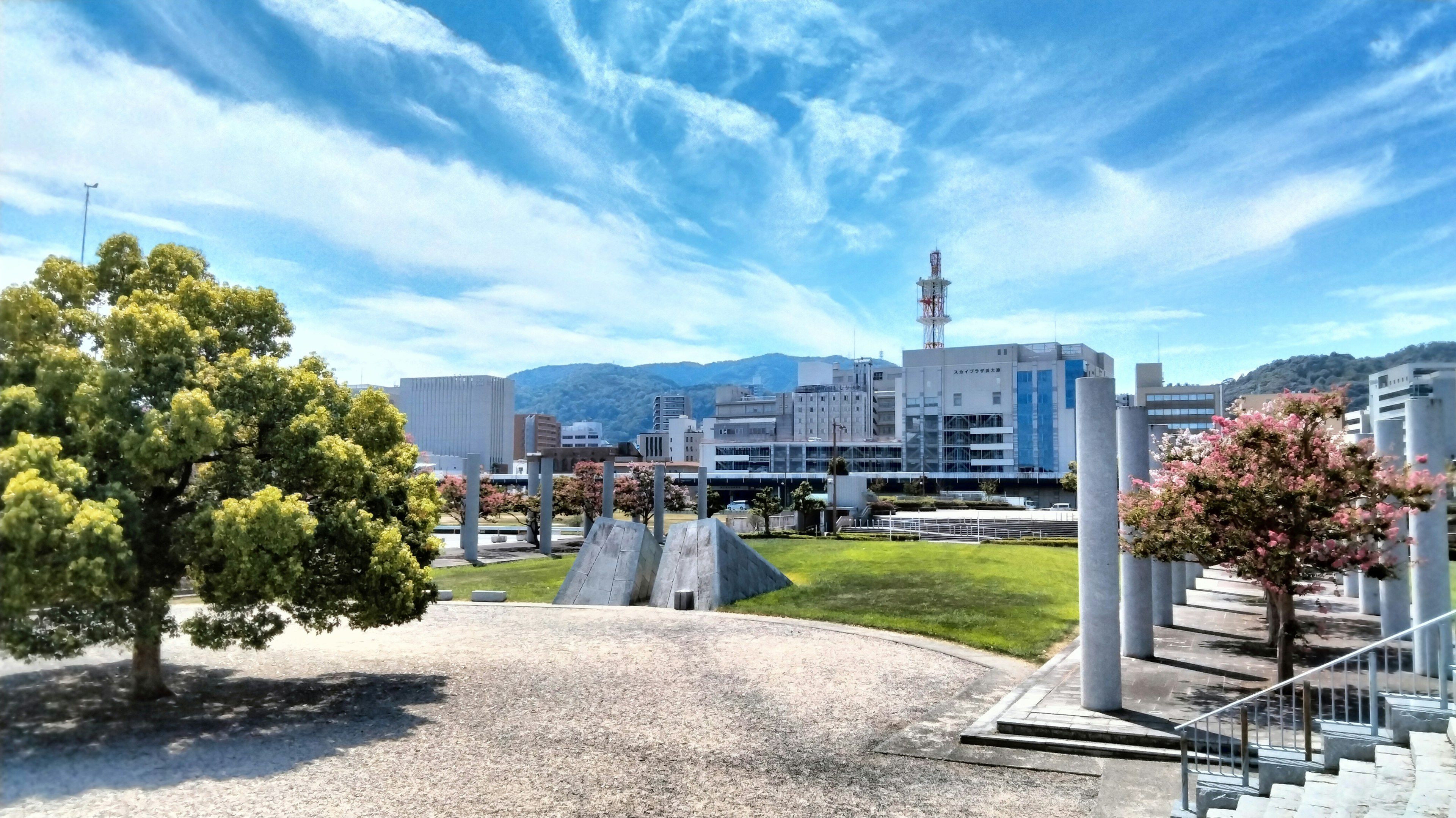 Park scene under a blue sky featuring modern buildings and sculptures