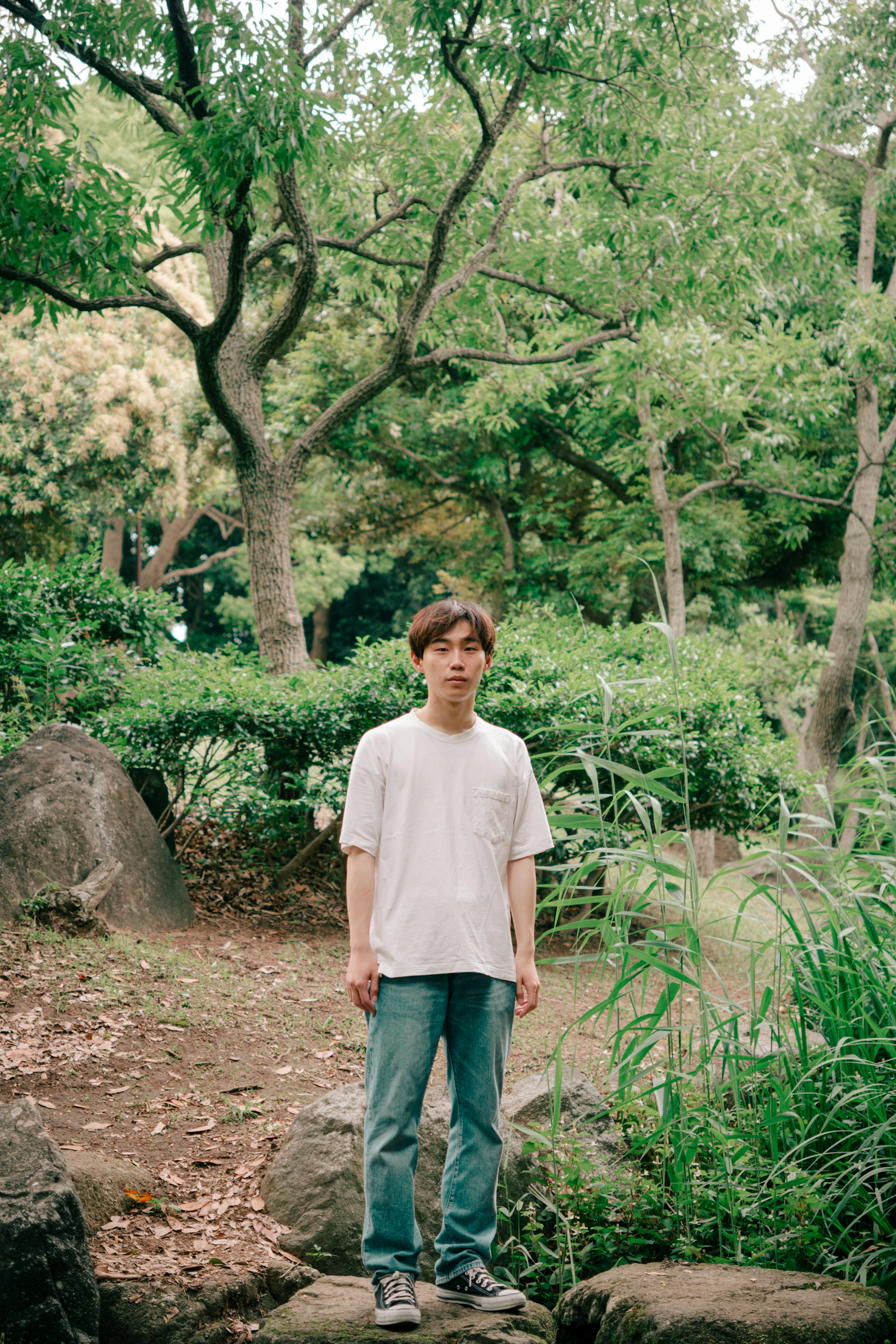 公園で立っている若い男性 緑の背景と石の上に立つ