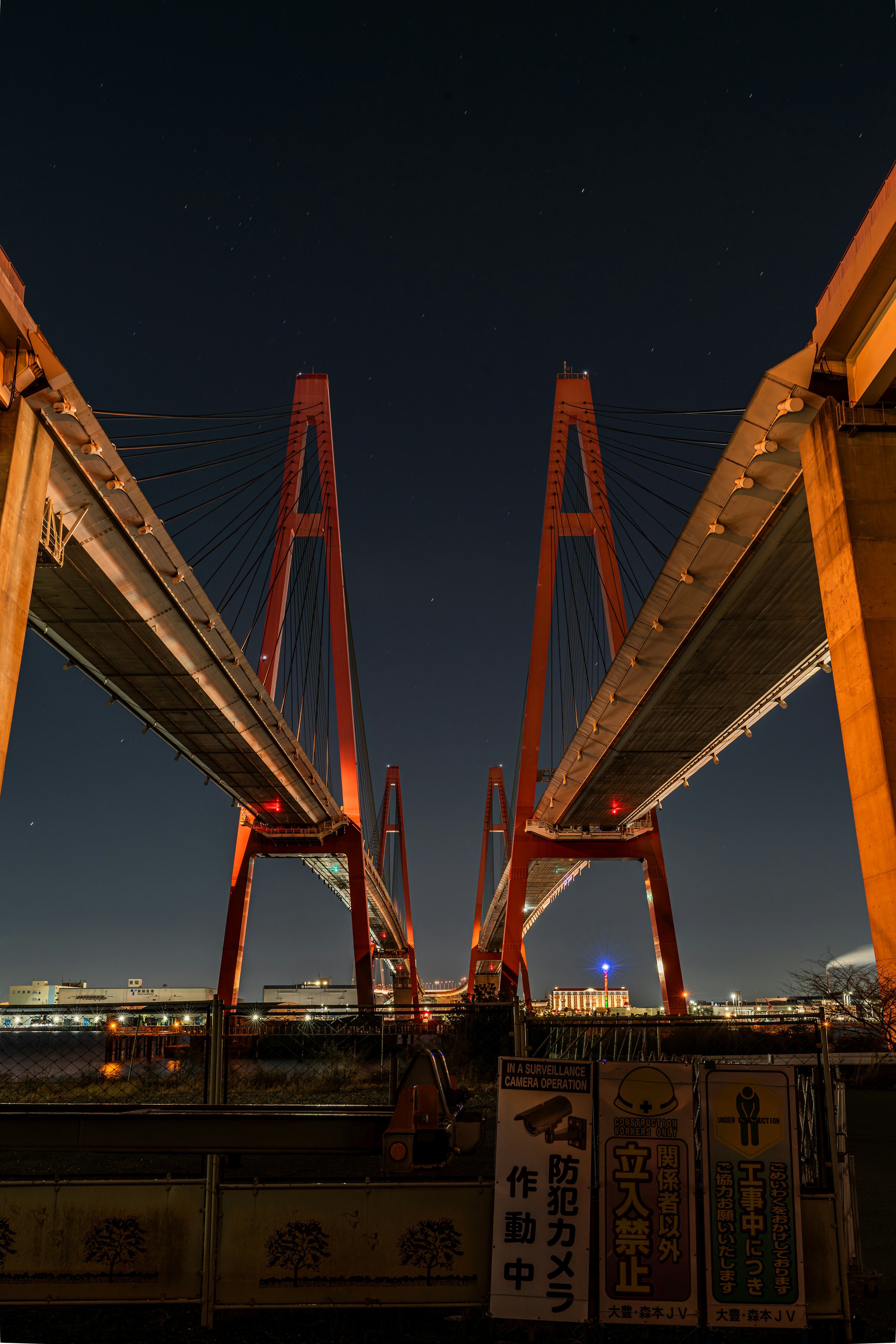 View from below a red suspension bridge at night highlighting its architectural features