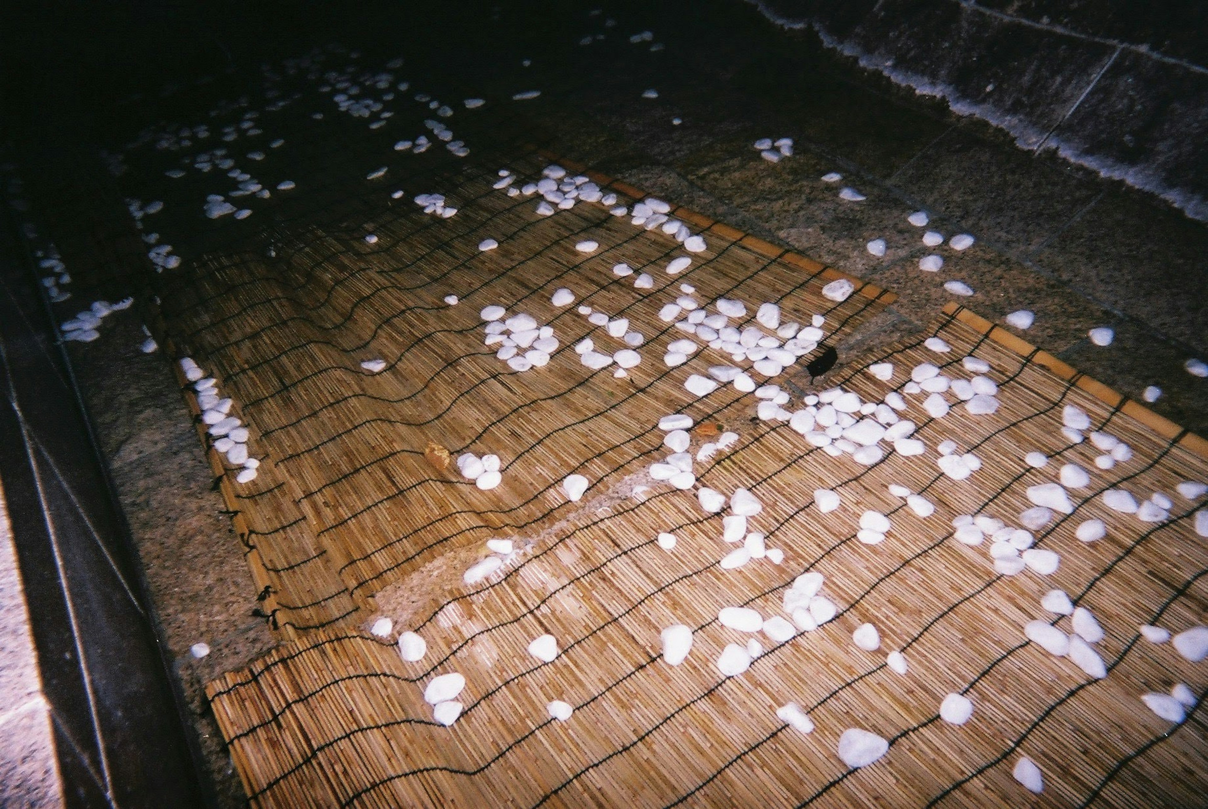 Un entorno oscuro con objetos blancos esparcidos sobre una estera tejida