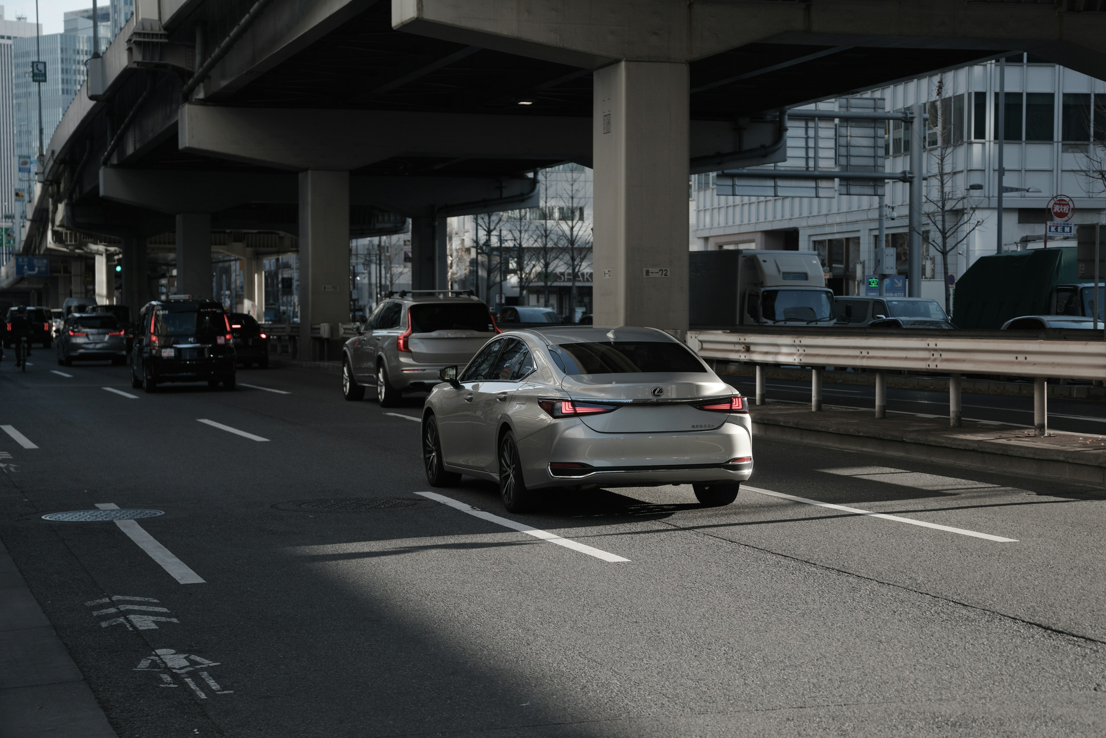 都市の道路を走る銀色の車と高架橋の風景