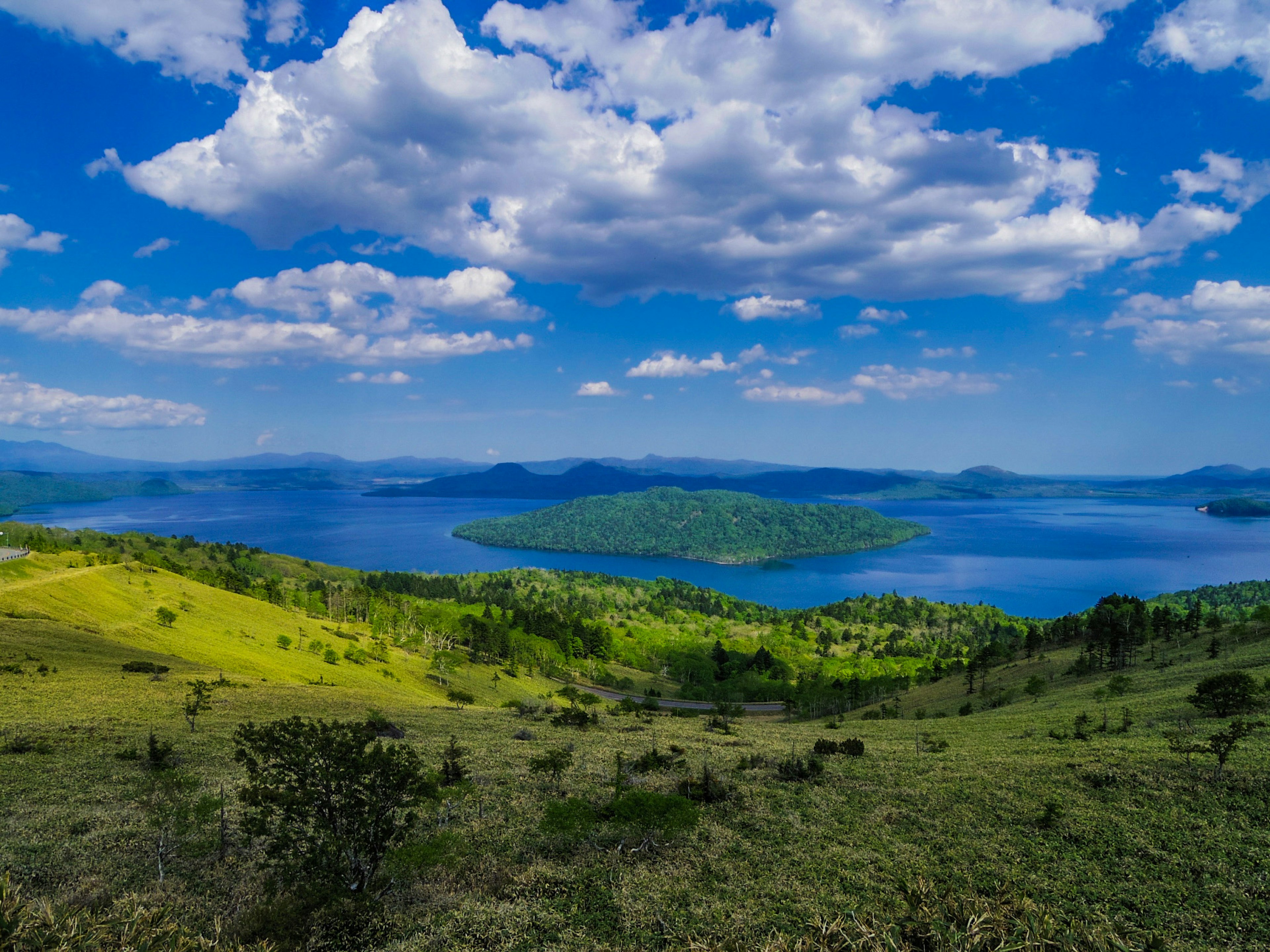 Malersiche Aussicht auf blauen Himmel und weiße Wolken über grünen Hügeln und einem See