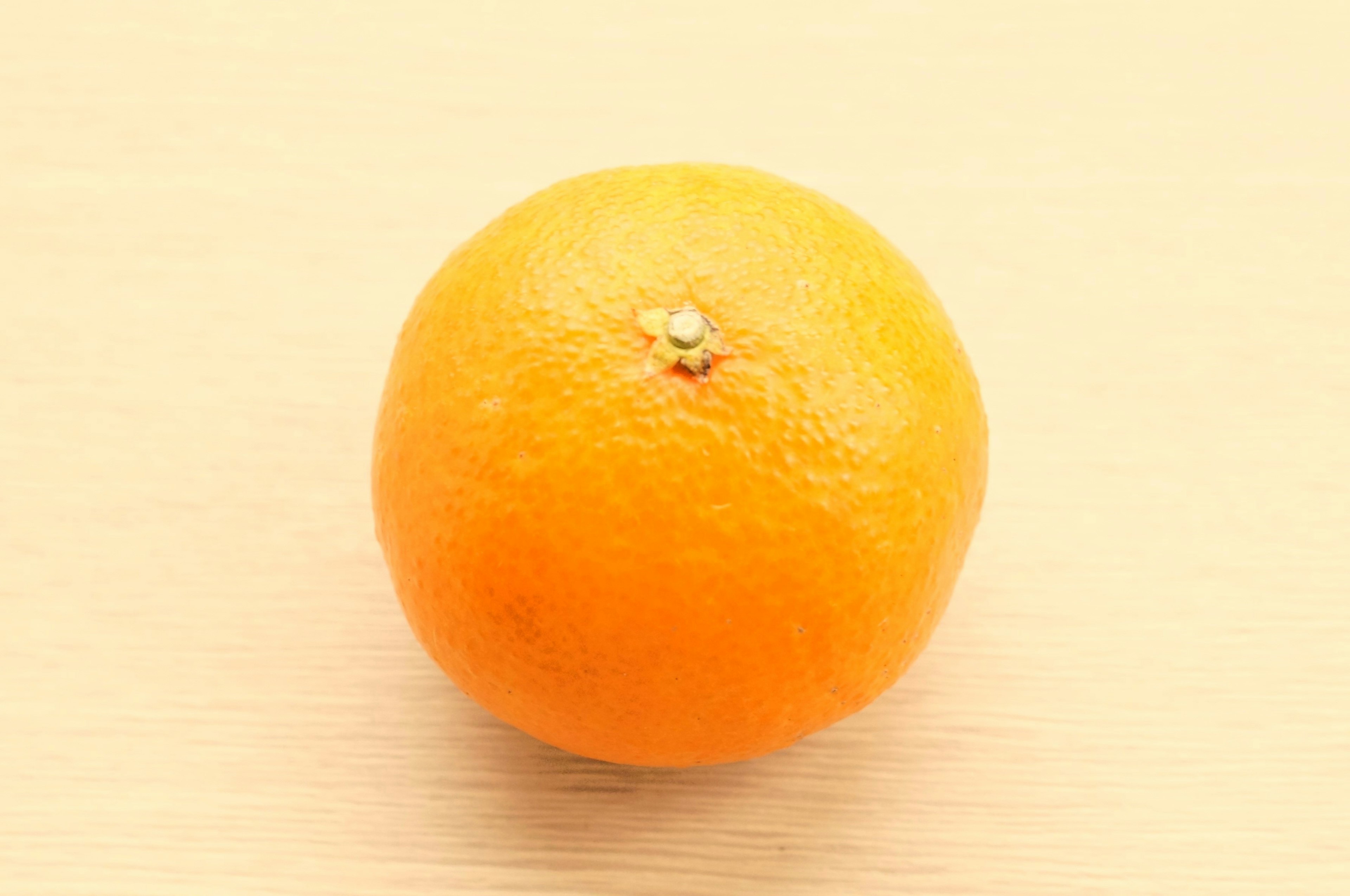 A fresh orange sitting on a light wooden surface