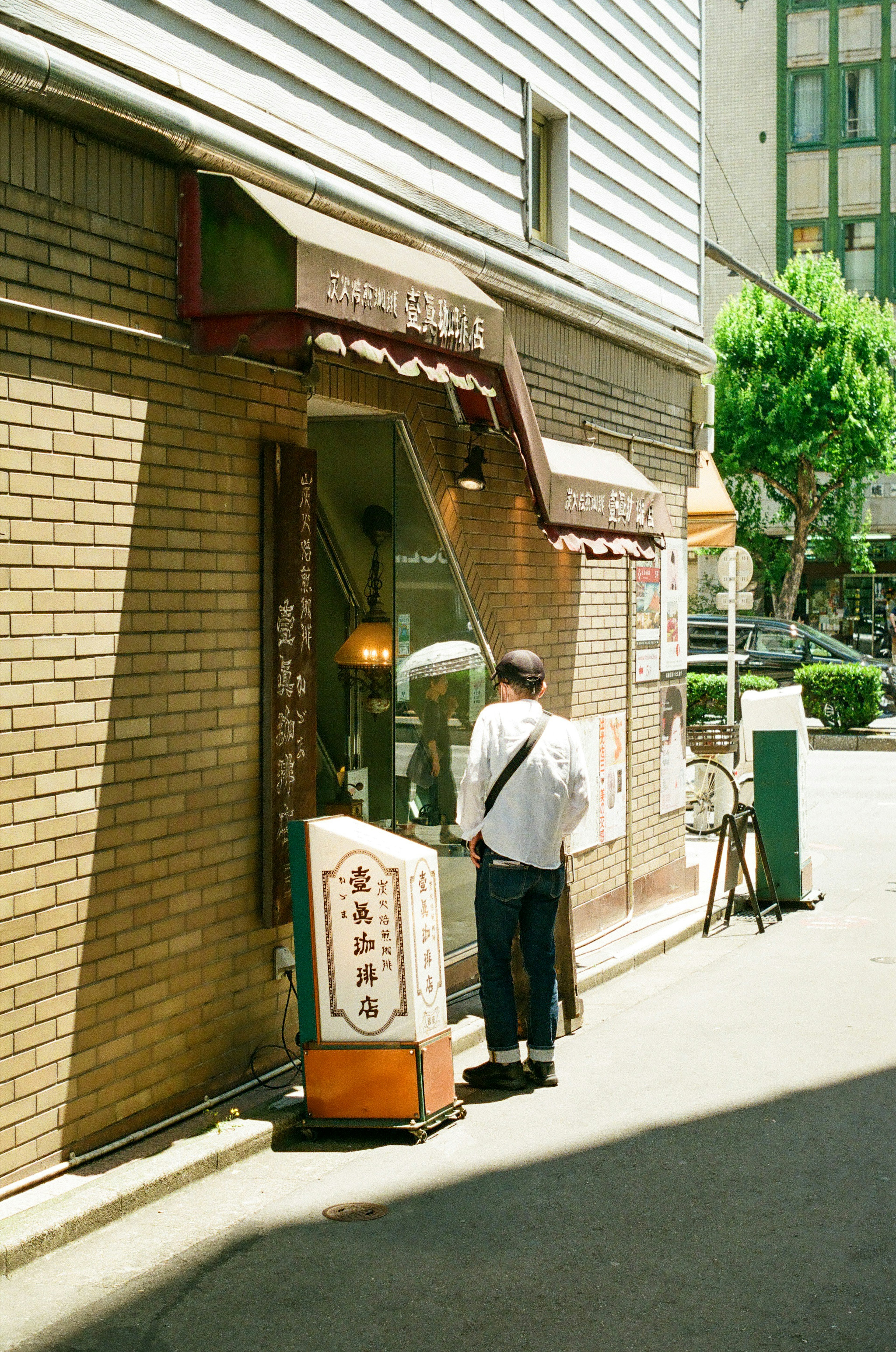 明るい通りにあるカフェの外観とその前に立つ人