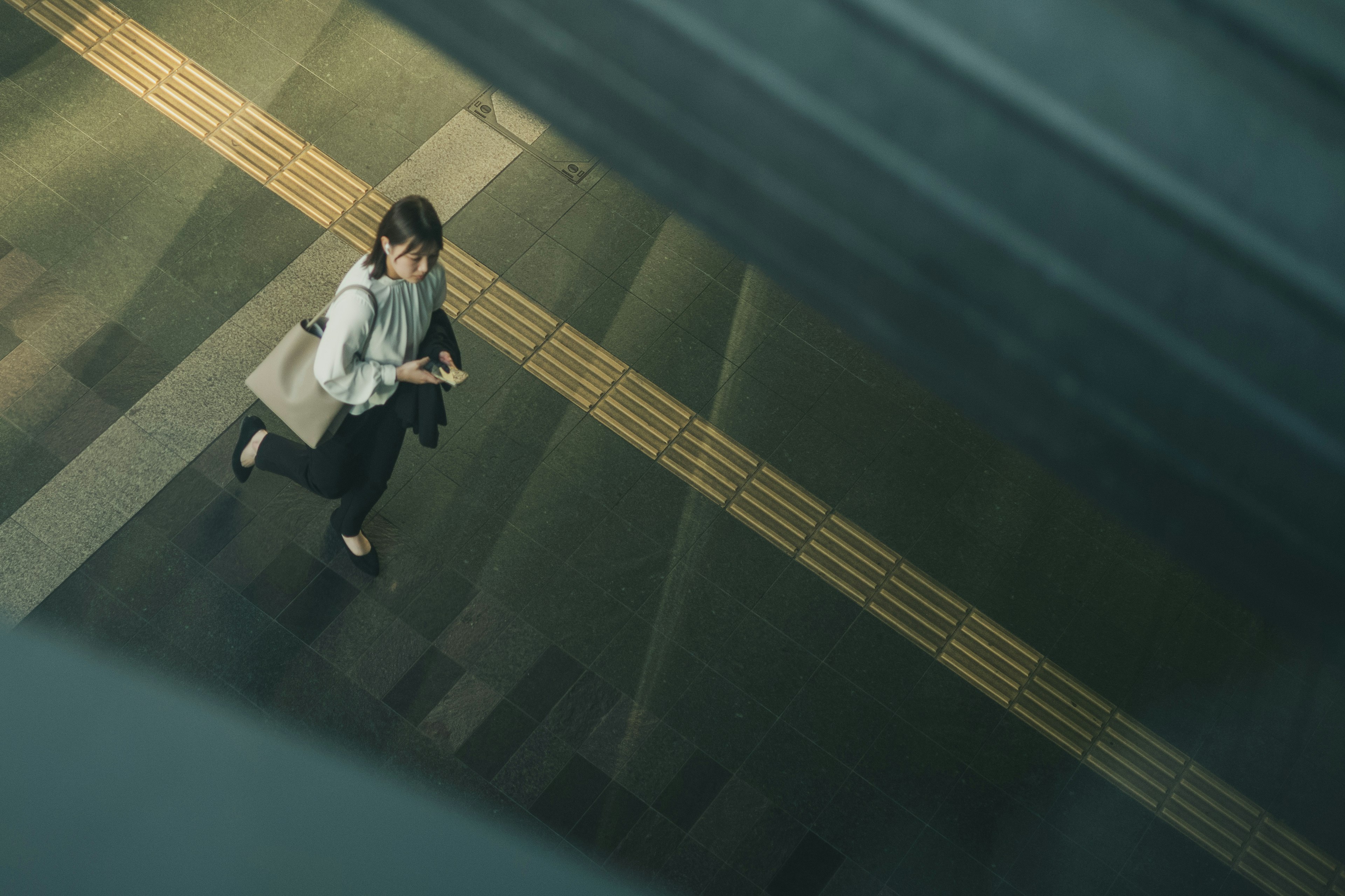 Vista dall'alto di una donna che scende le scale con una borsa e controlla il suo smartphone