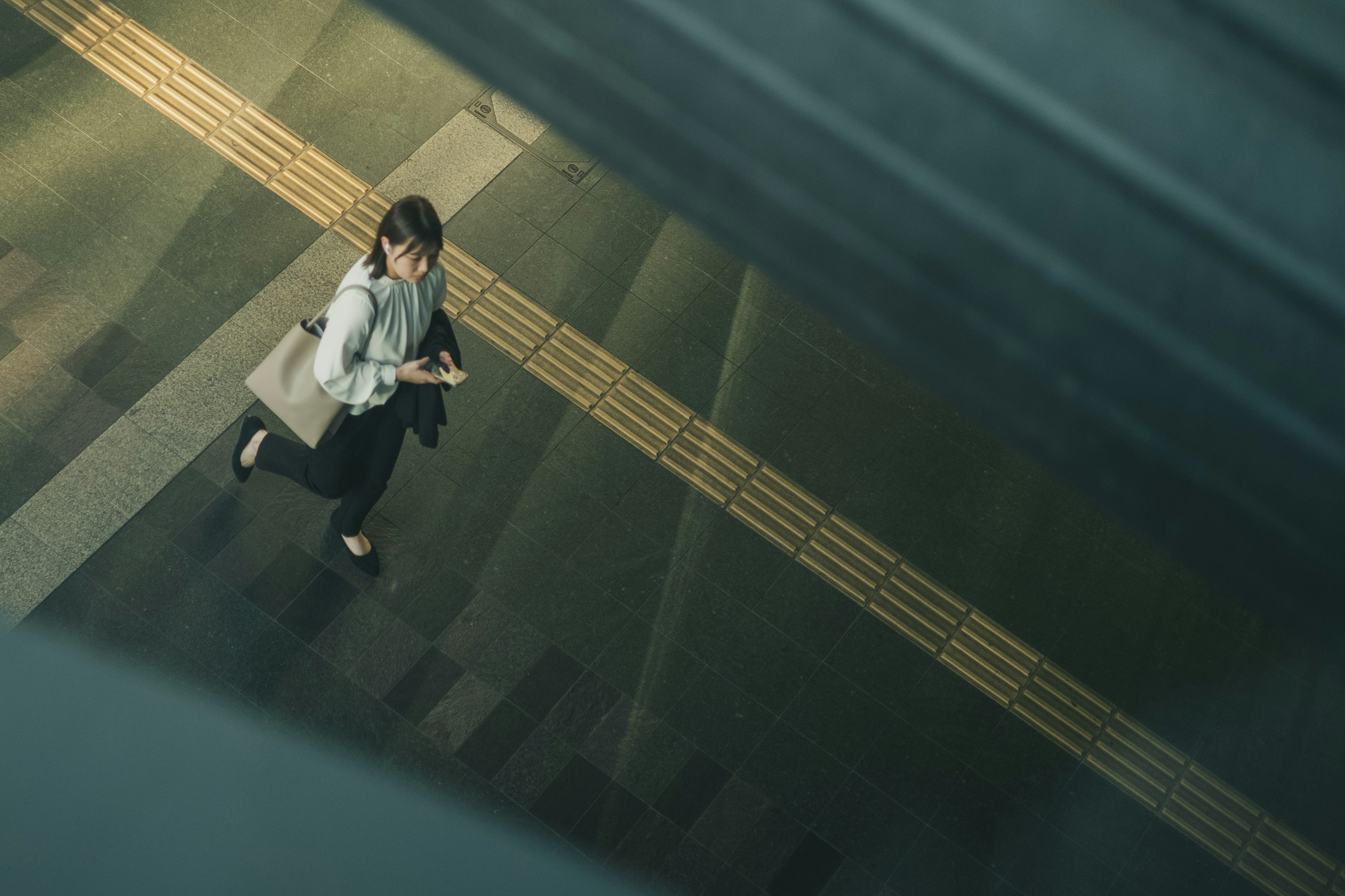 Top view of a woman walking down stairs carrying a bag and checking her smartphone