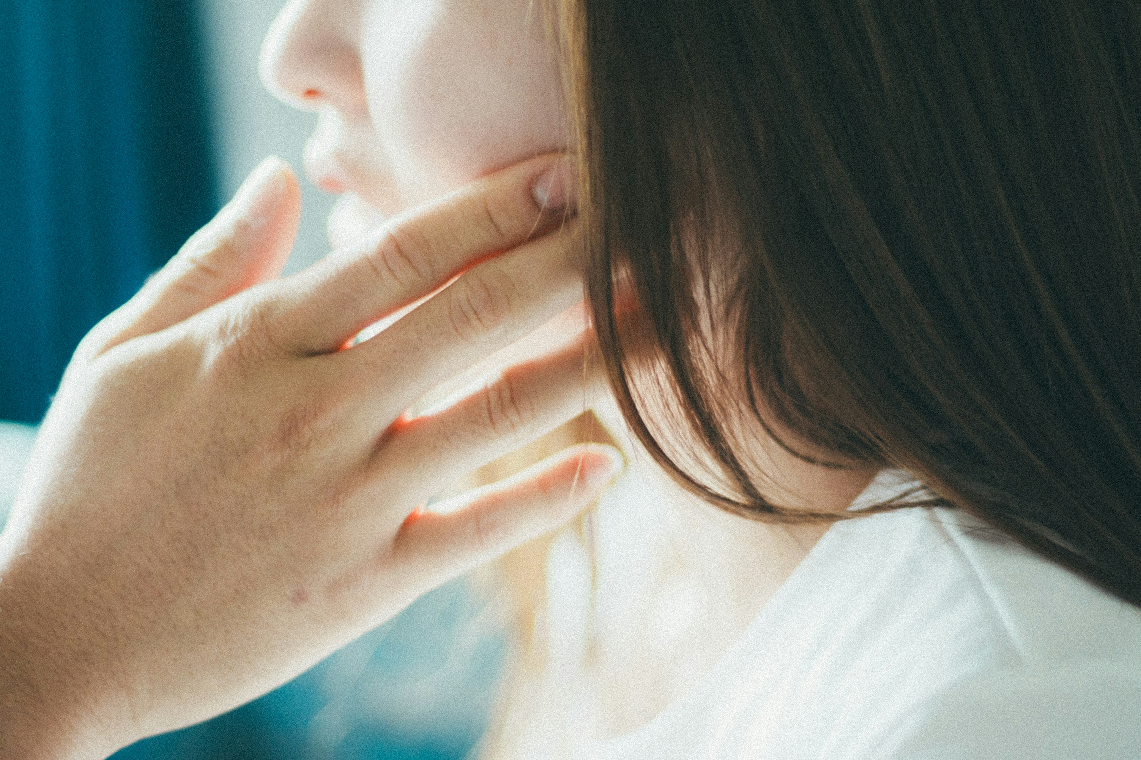 Une main touchant doucement le côté du visage d'une femme dans un cadre serein avec un éclairage doux