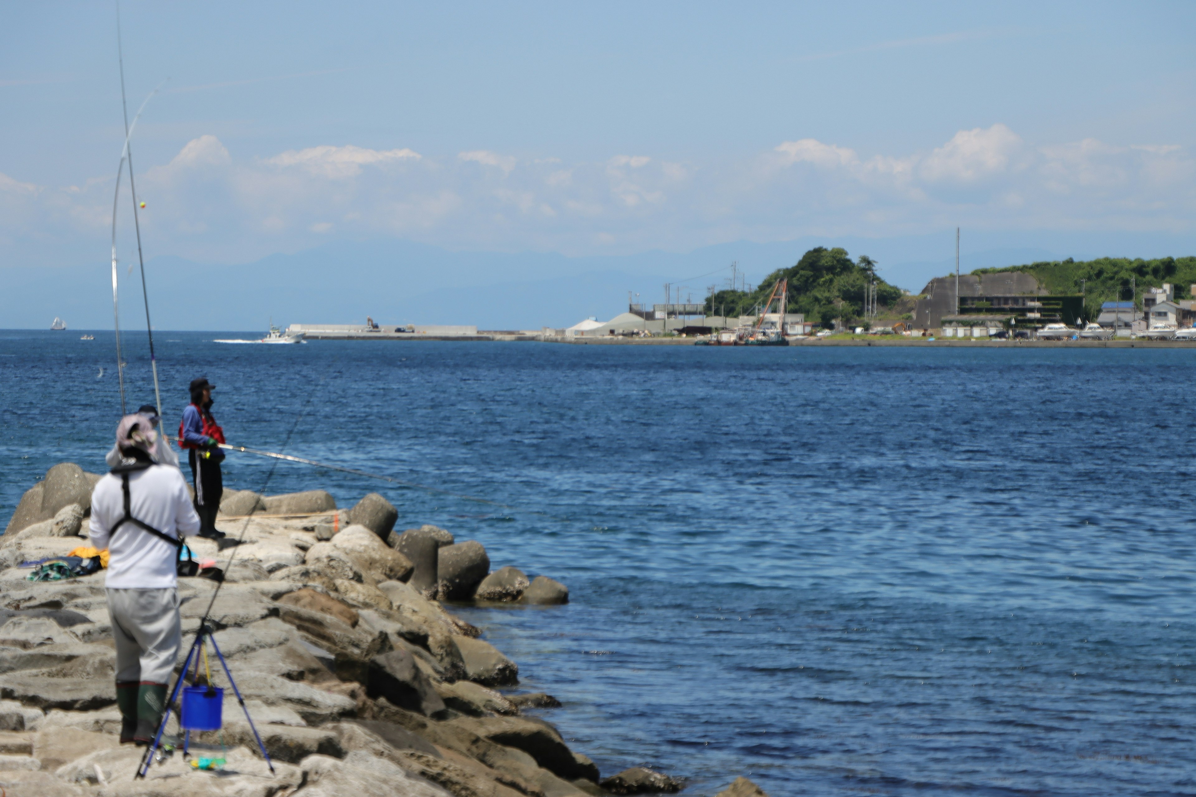 Two men fishing on a rocky shore with a blue ocean