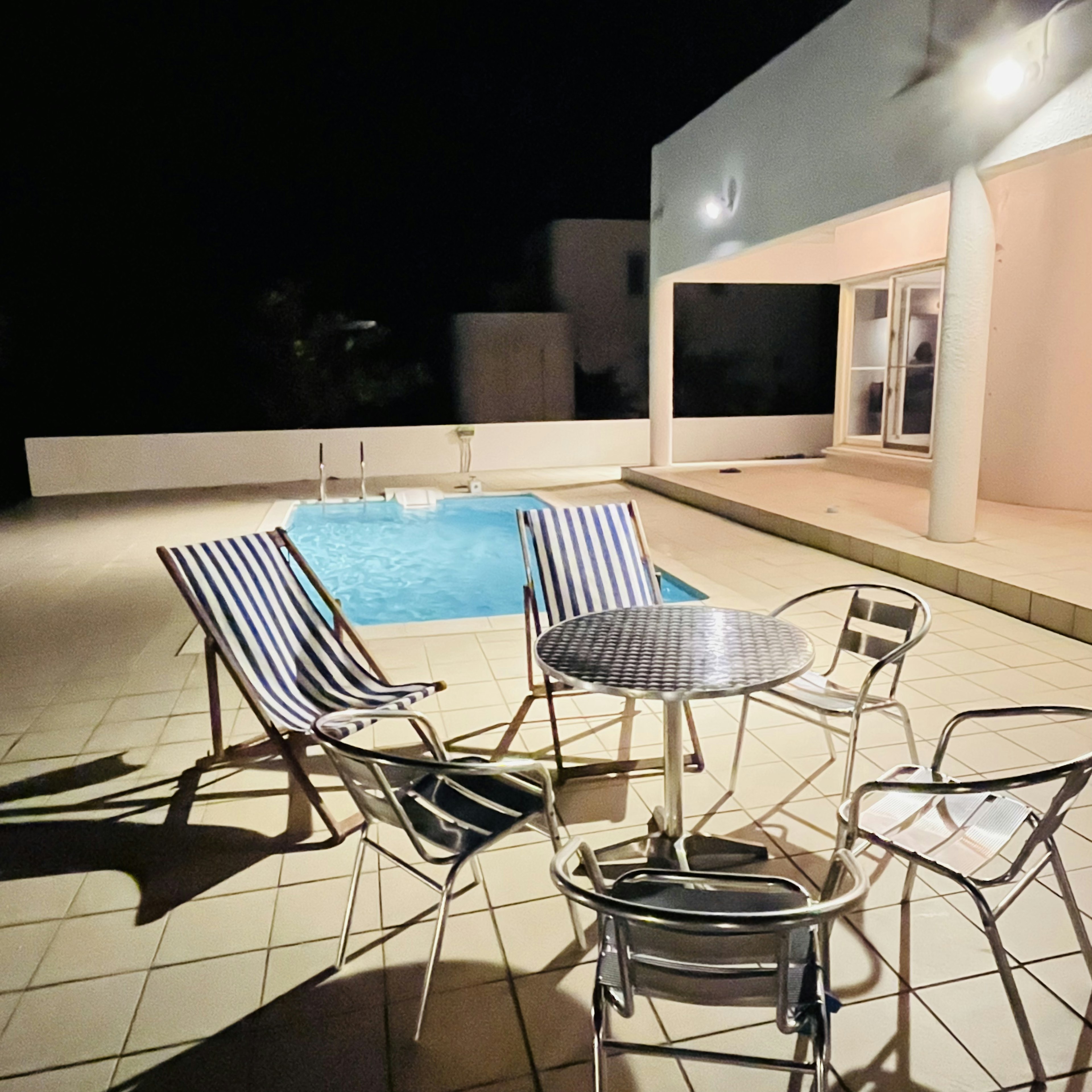 Espace de détente au bord de la piscine avec des chaises rayées et une table la nuit