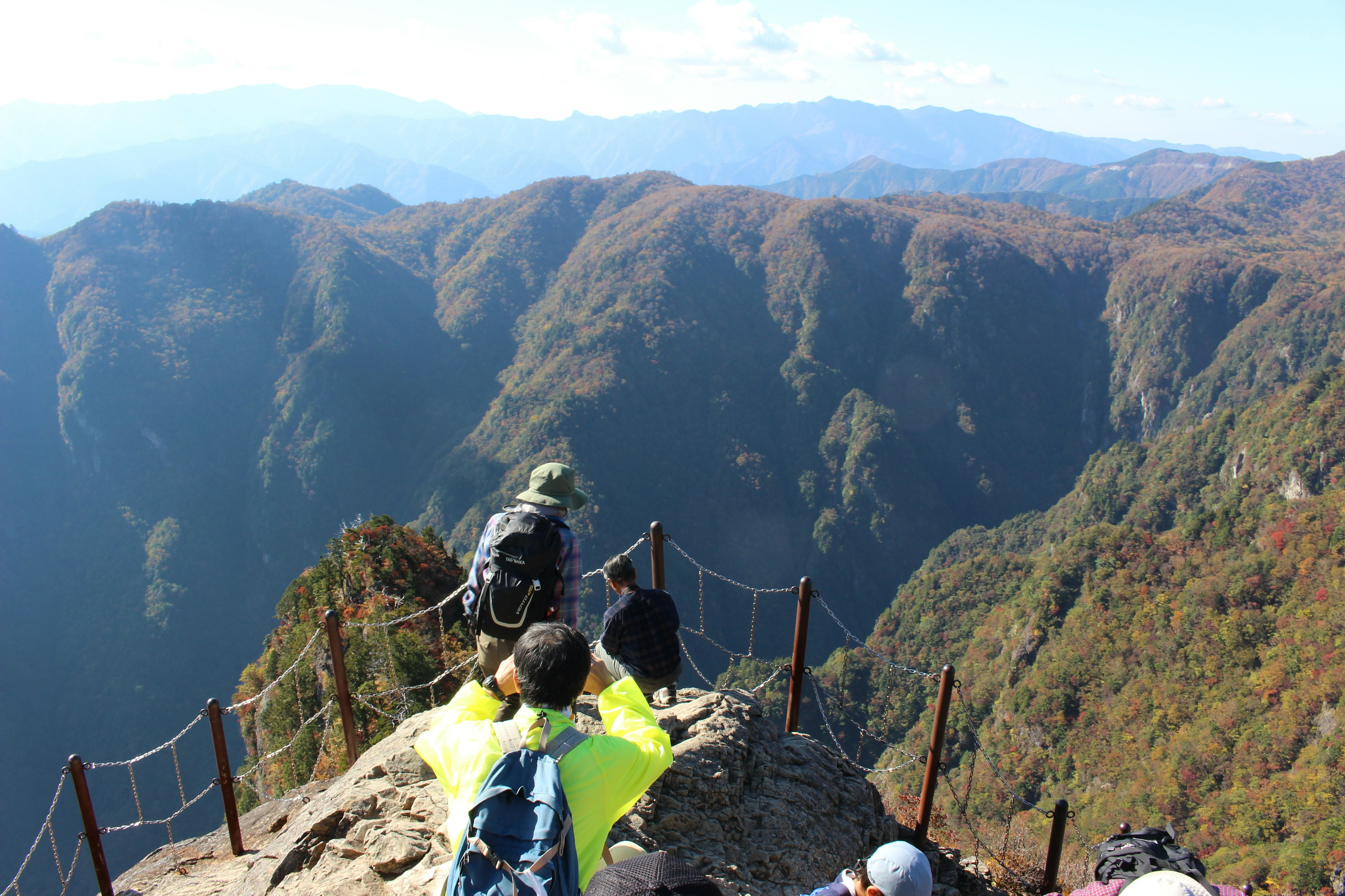 Orang-orang berdiri di puncak gunung menghadap ke pegunungan yang indah