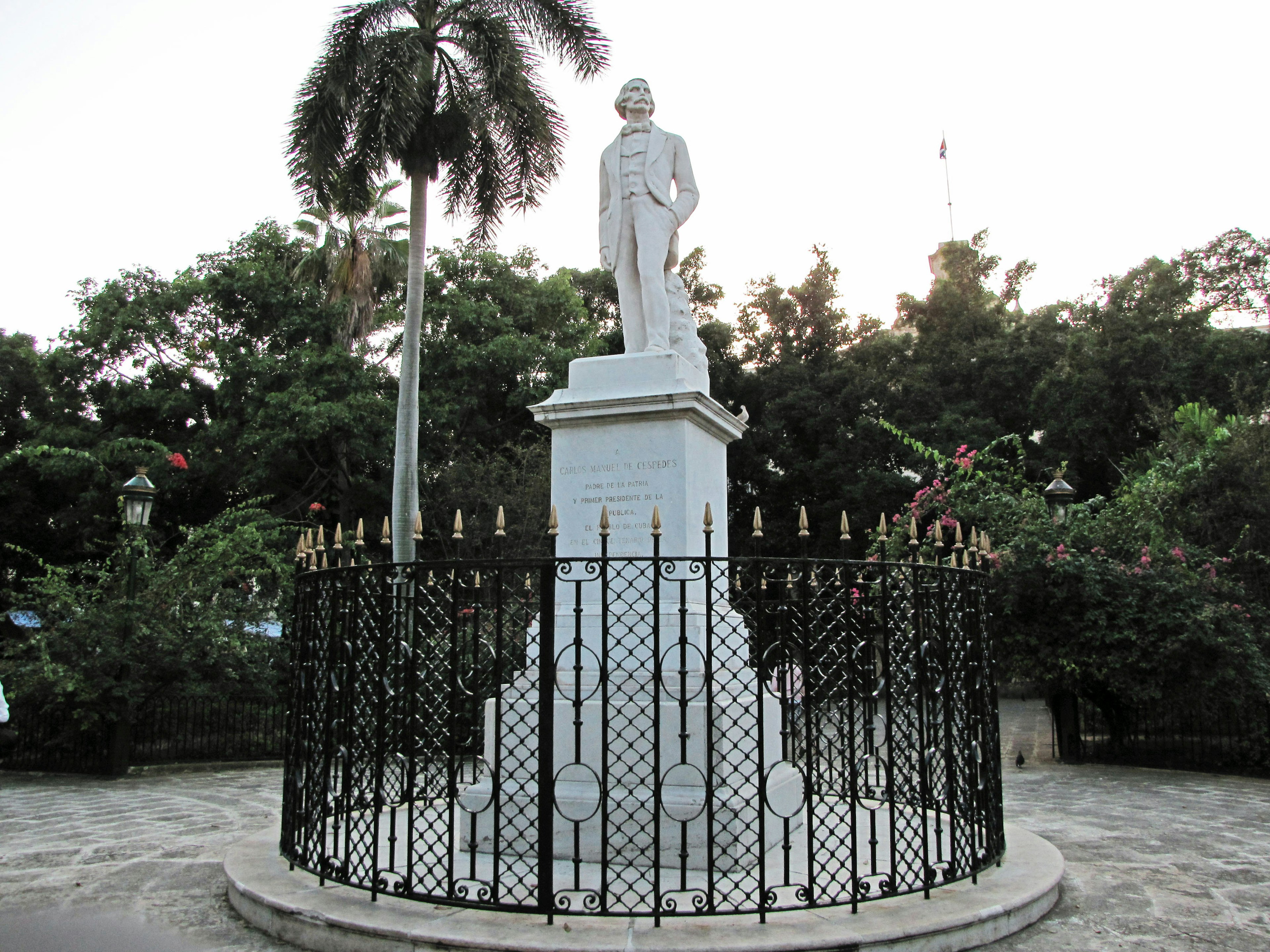 Monument with a white statue surrounded by a decorative black fence in a park