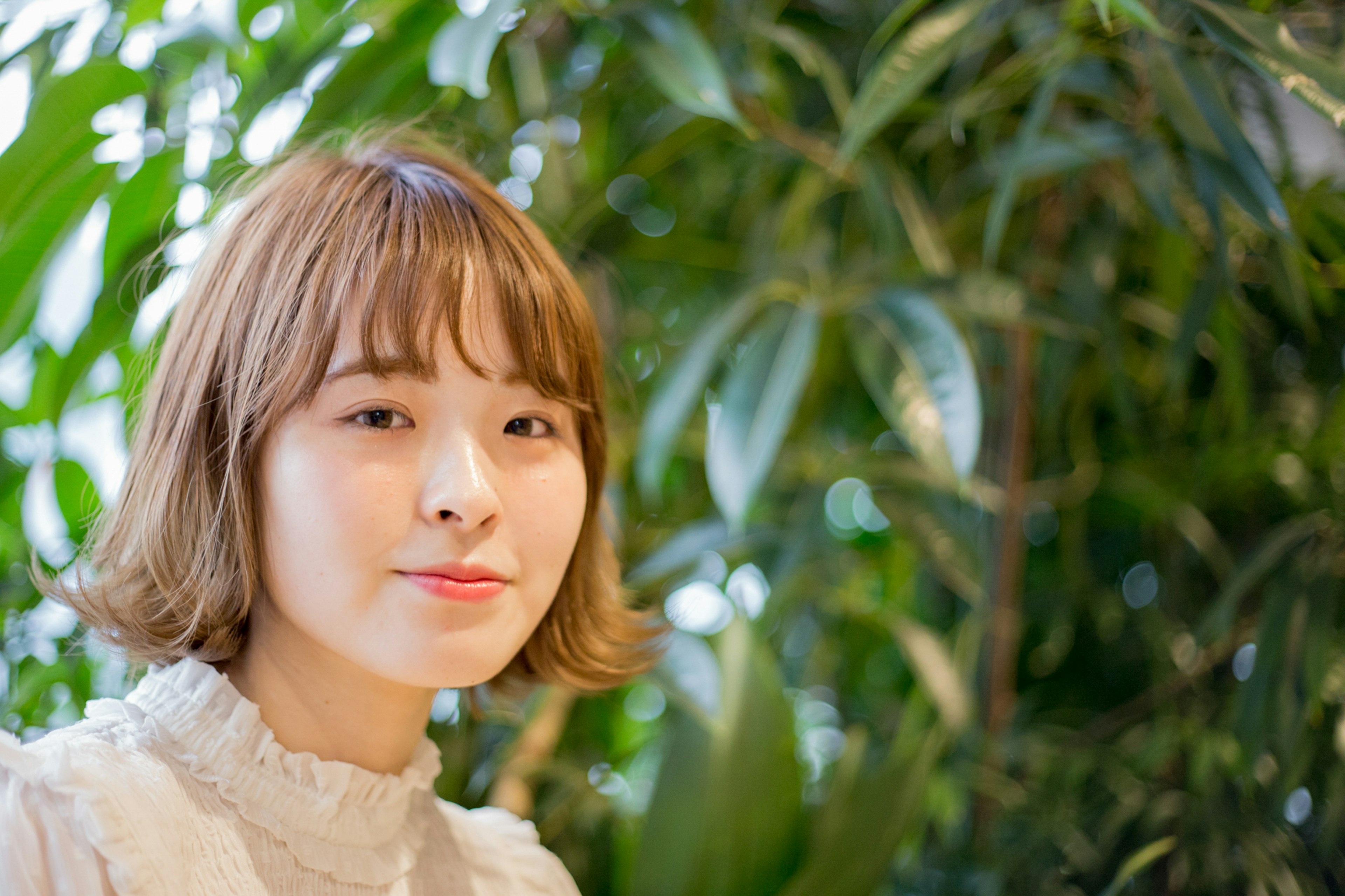 Portrait of a woman in front of green plants with short hair and a smiling expression