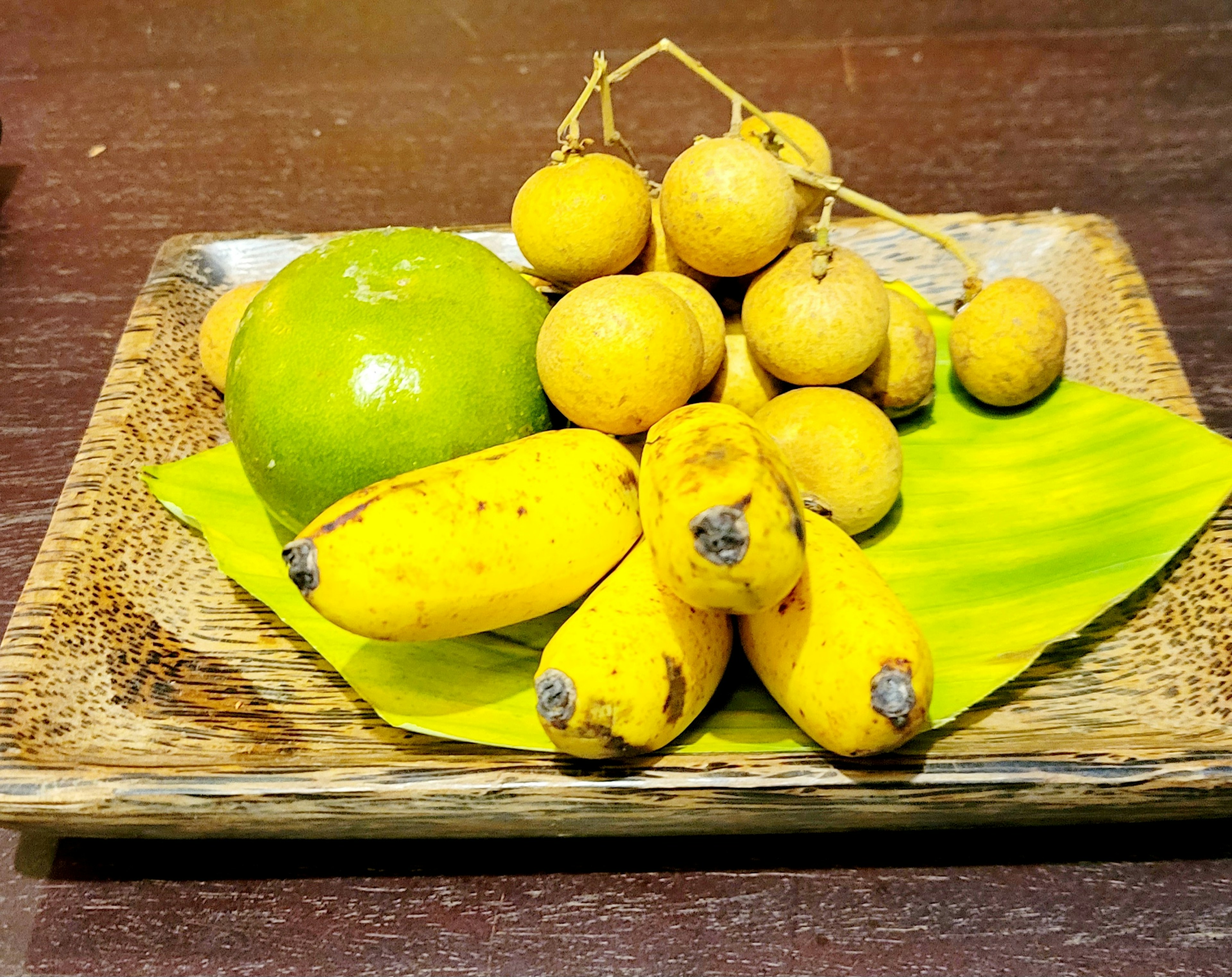 Un plato con plátanos amarillos una manzana verde y frutas redondas que parecen lichis