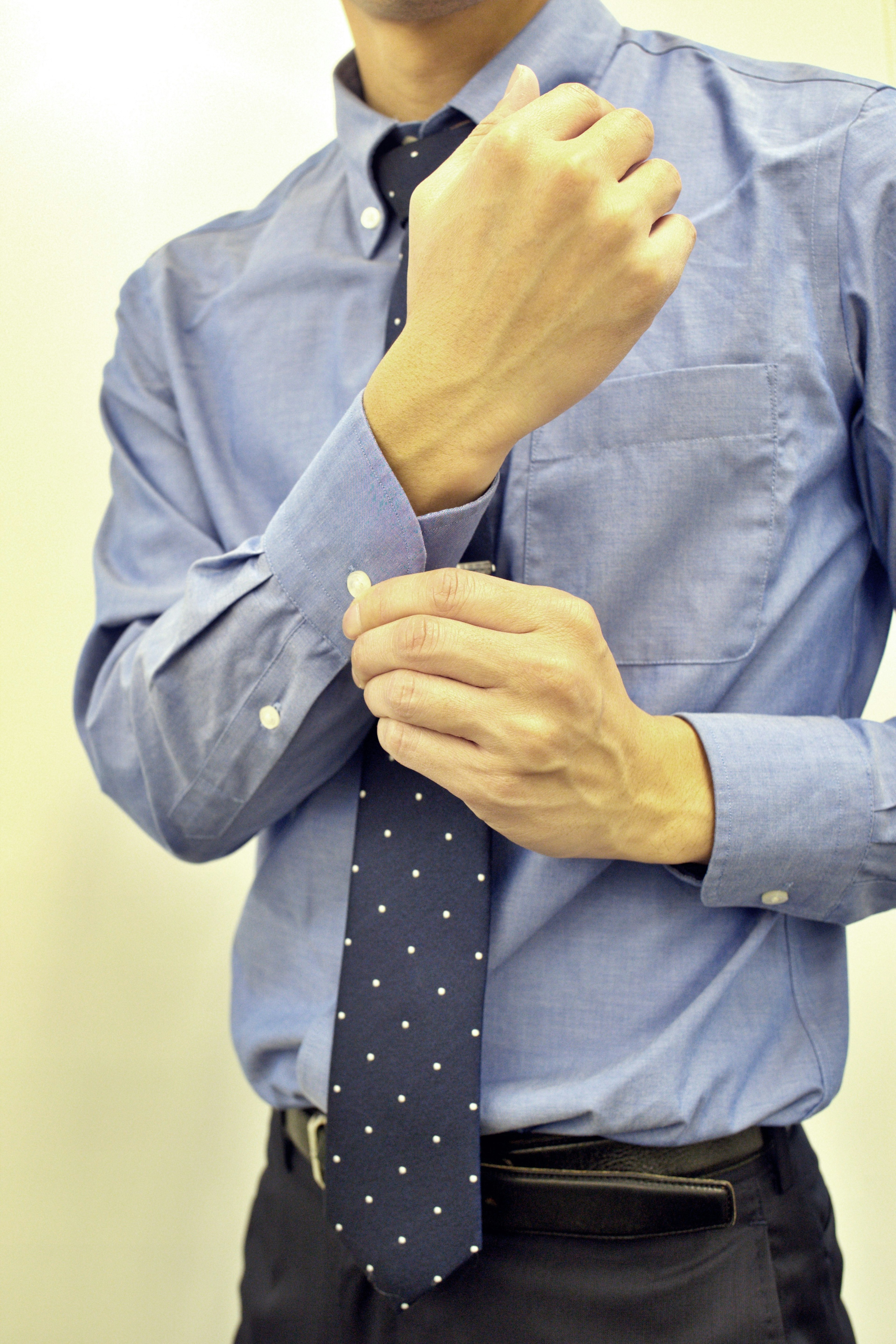 Hombre con camisa azul ajustando su puño mientras se prepara para anudar una corbata de lunares