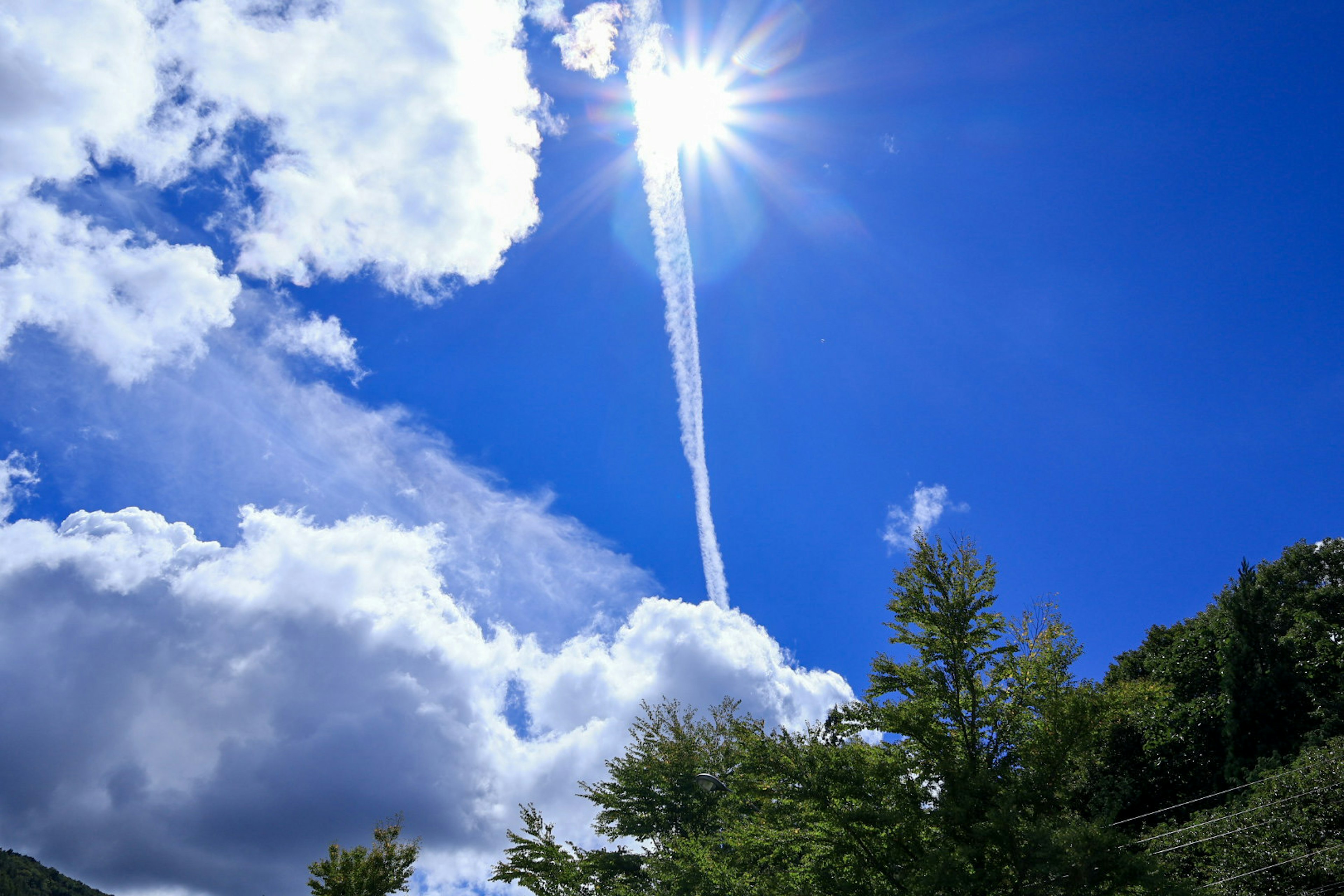 Bright sunlight shining through clouds with a contrail