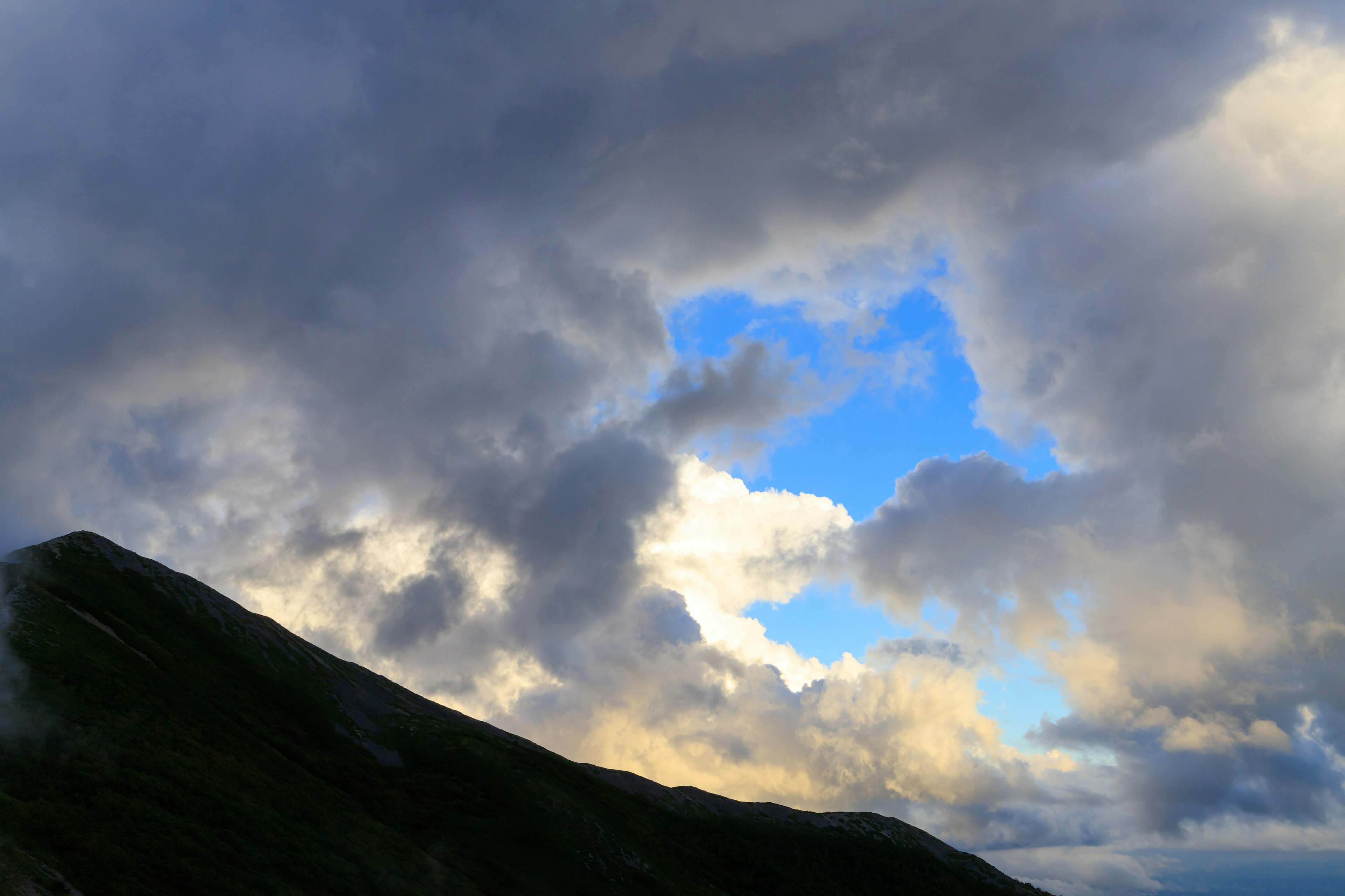 Silhouette gunung dengan langit biru terlihat di antara awan