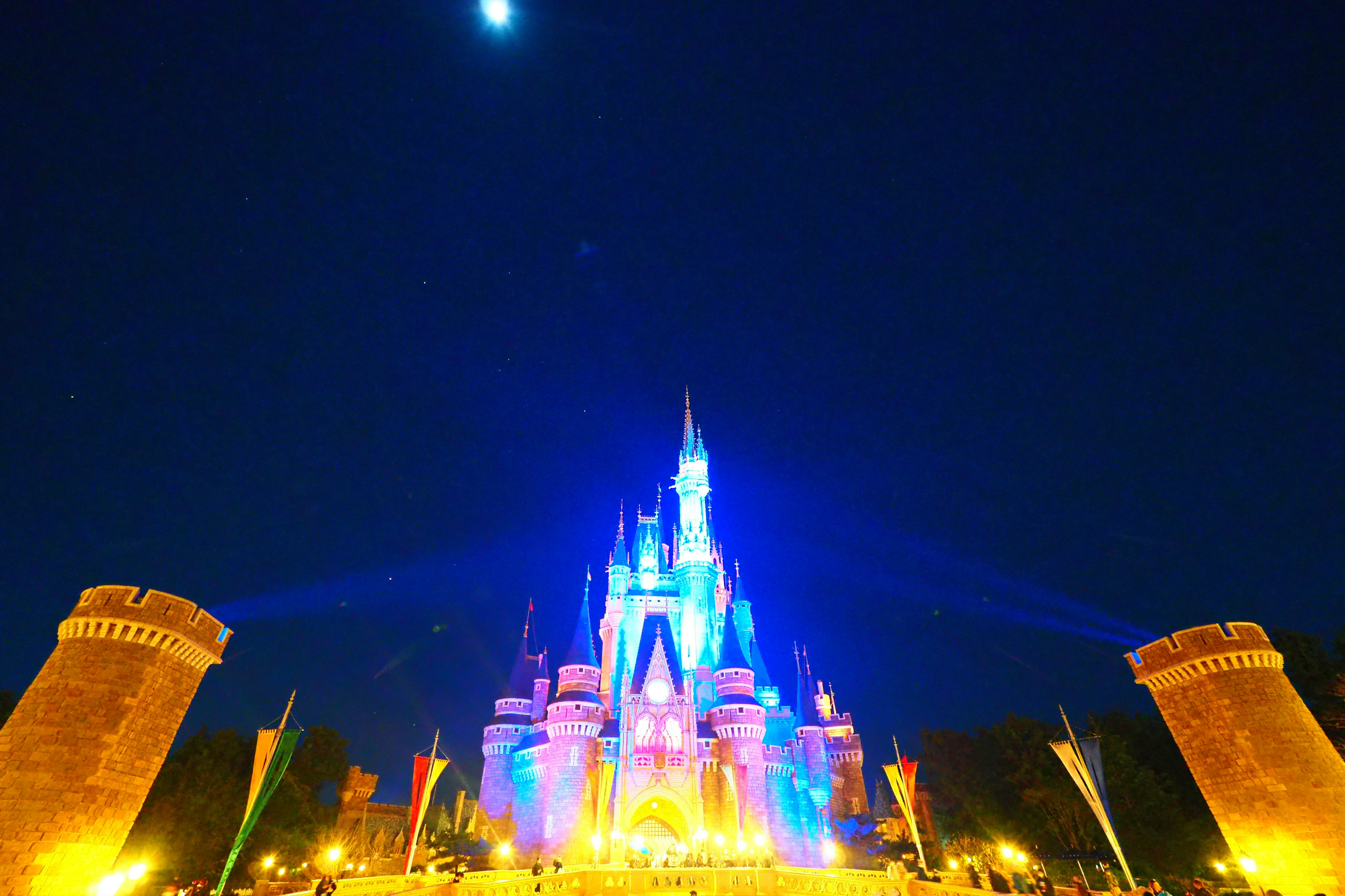 Castillo de Disney colorido iluminado por la noche con una luna brillante