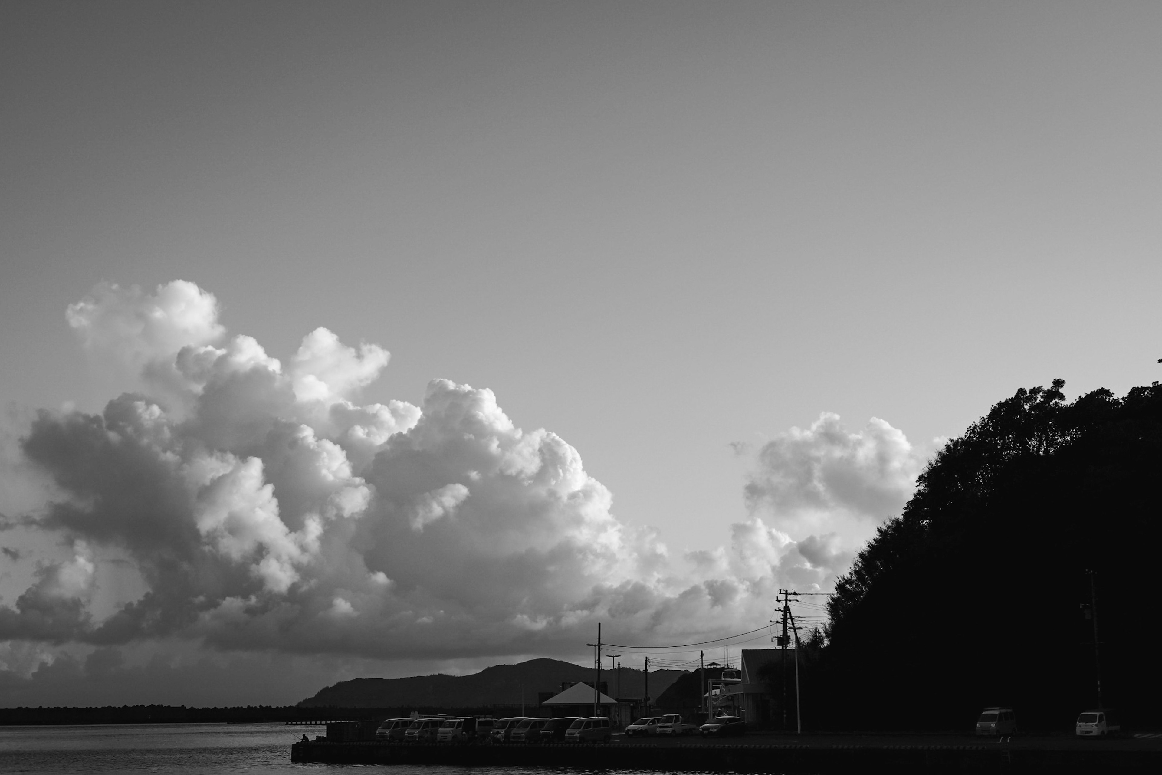 Paysage côtier en noir et blanc avec des nuages et des montagnes sur une surface d'eau calme