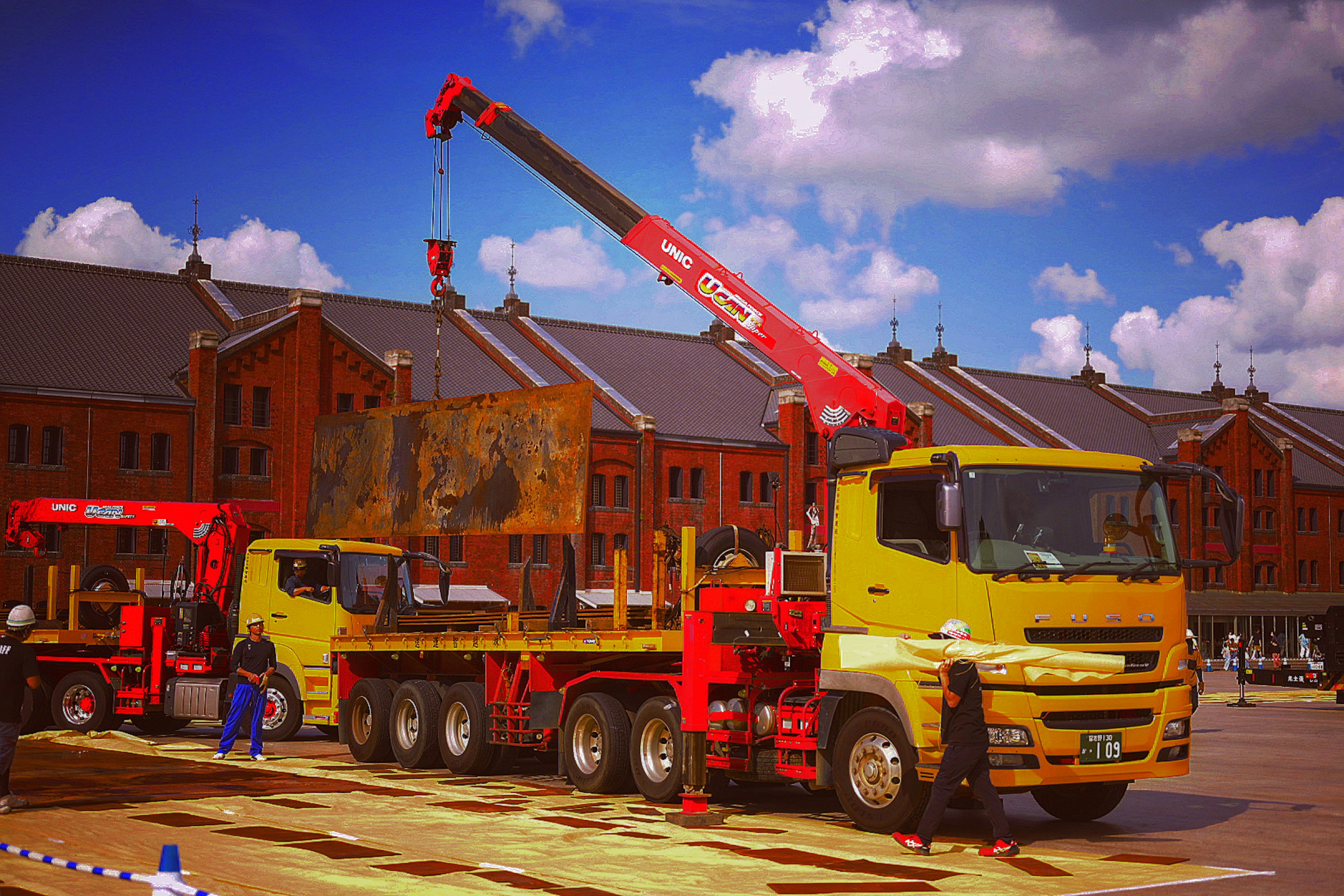 Camion jaune avec grue rouge soulevant une grande charge en extérieur