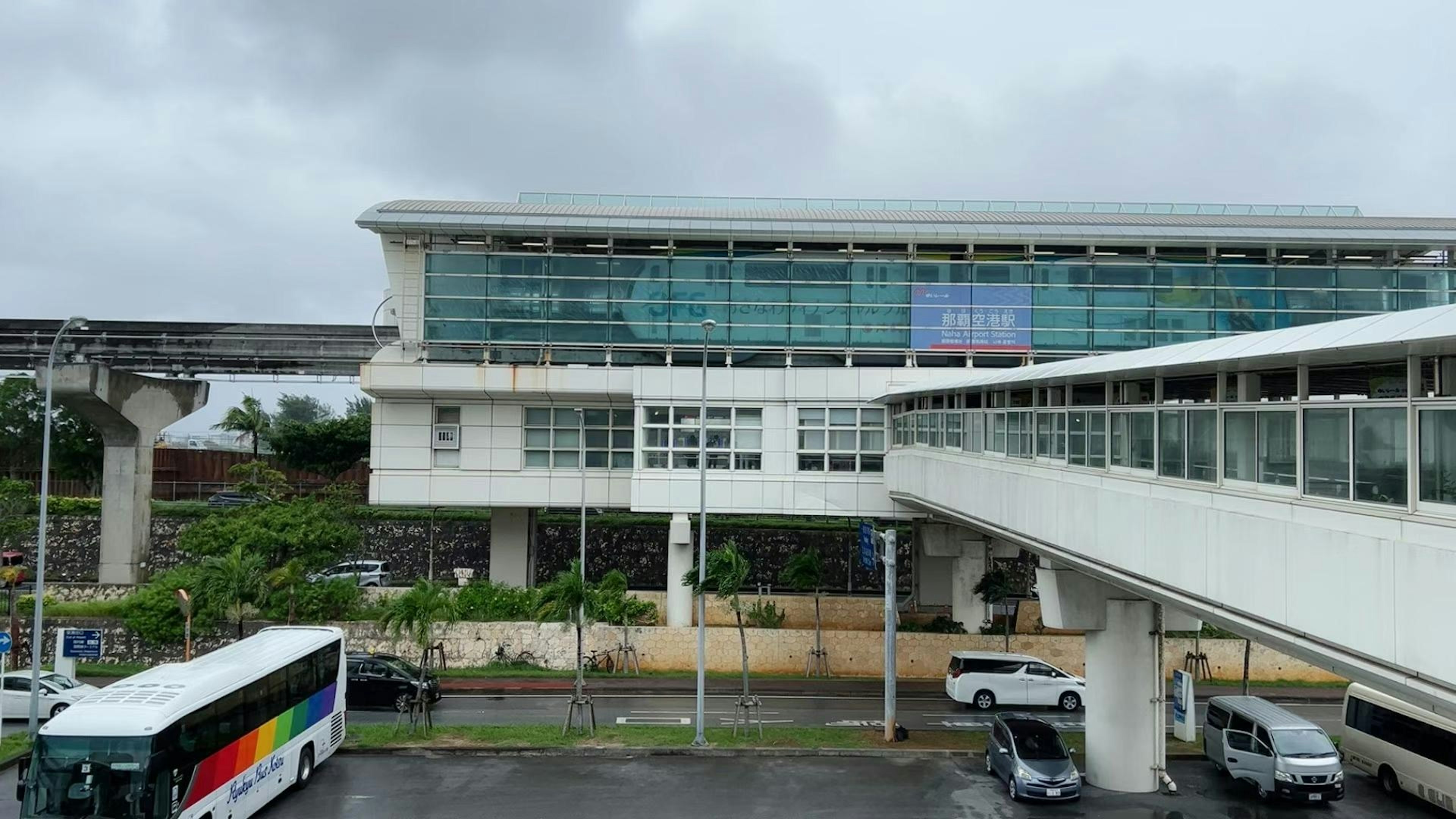 Modern train station building with a monorail overhead under cloudy skies