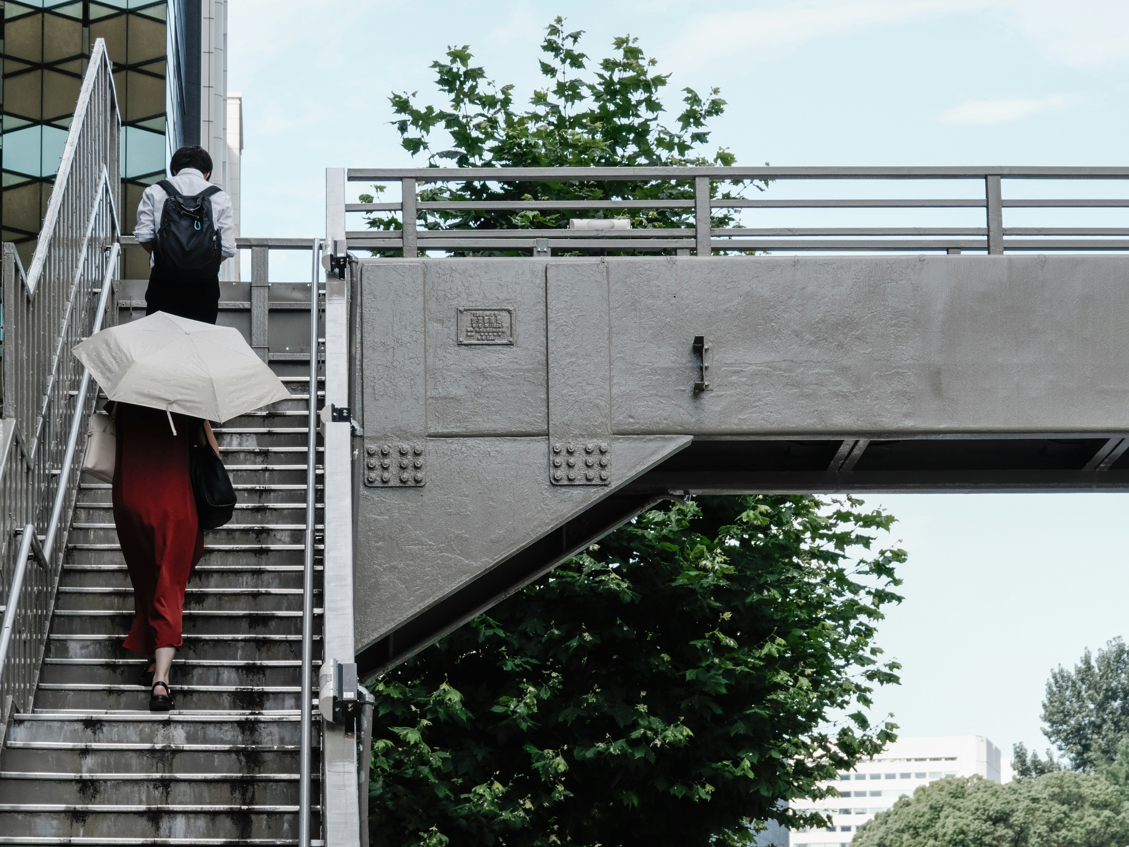 Una mujer con un vestido rojo subiendo escaleras mientras un hombre lleva un paraguas