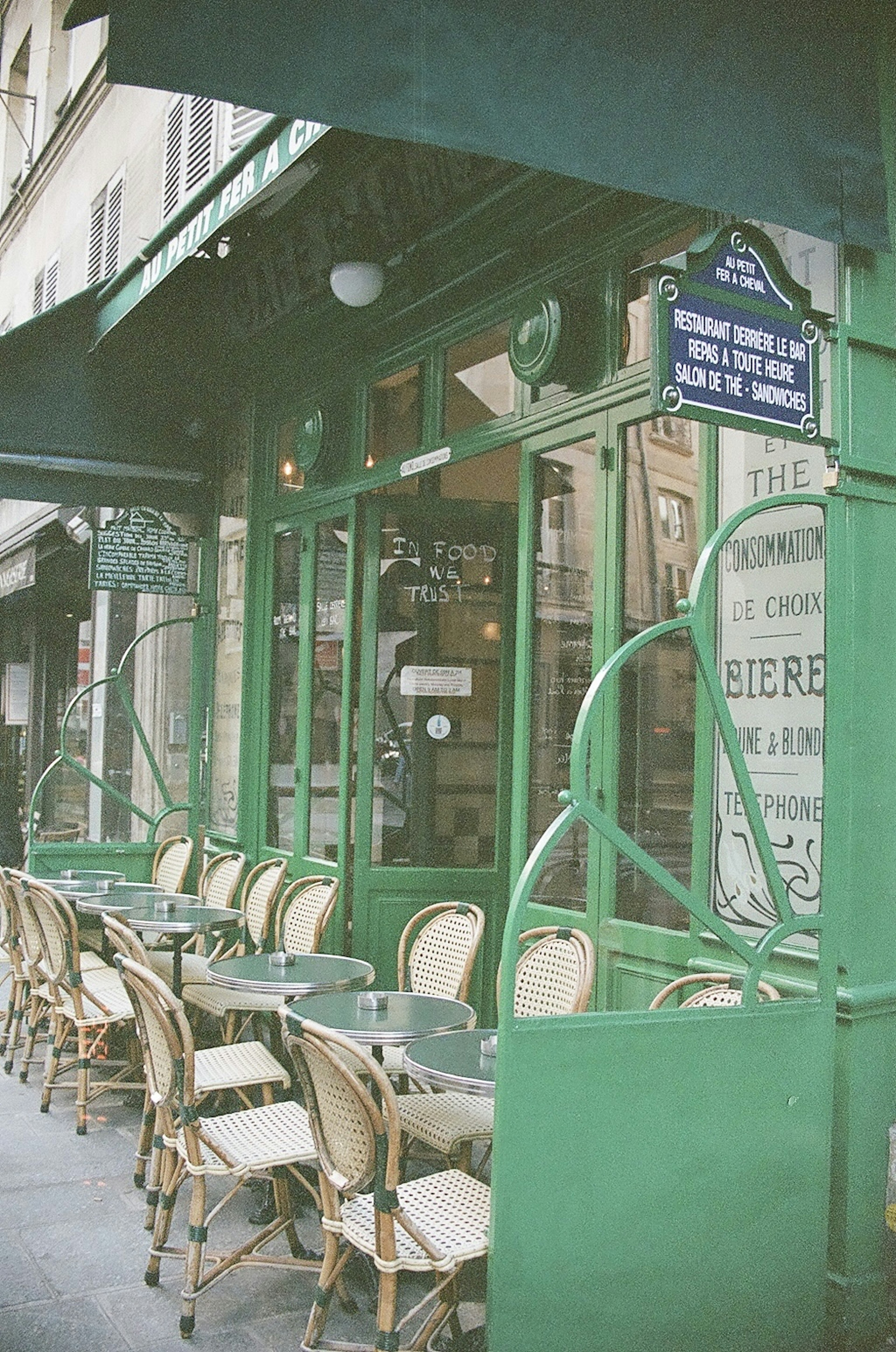 Entrée d'un café parisien avec une façade verte chaises soigneusement disposées