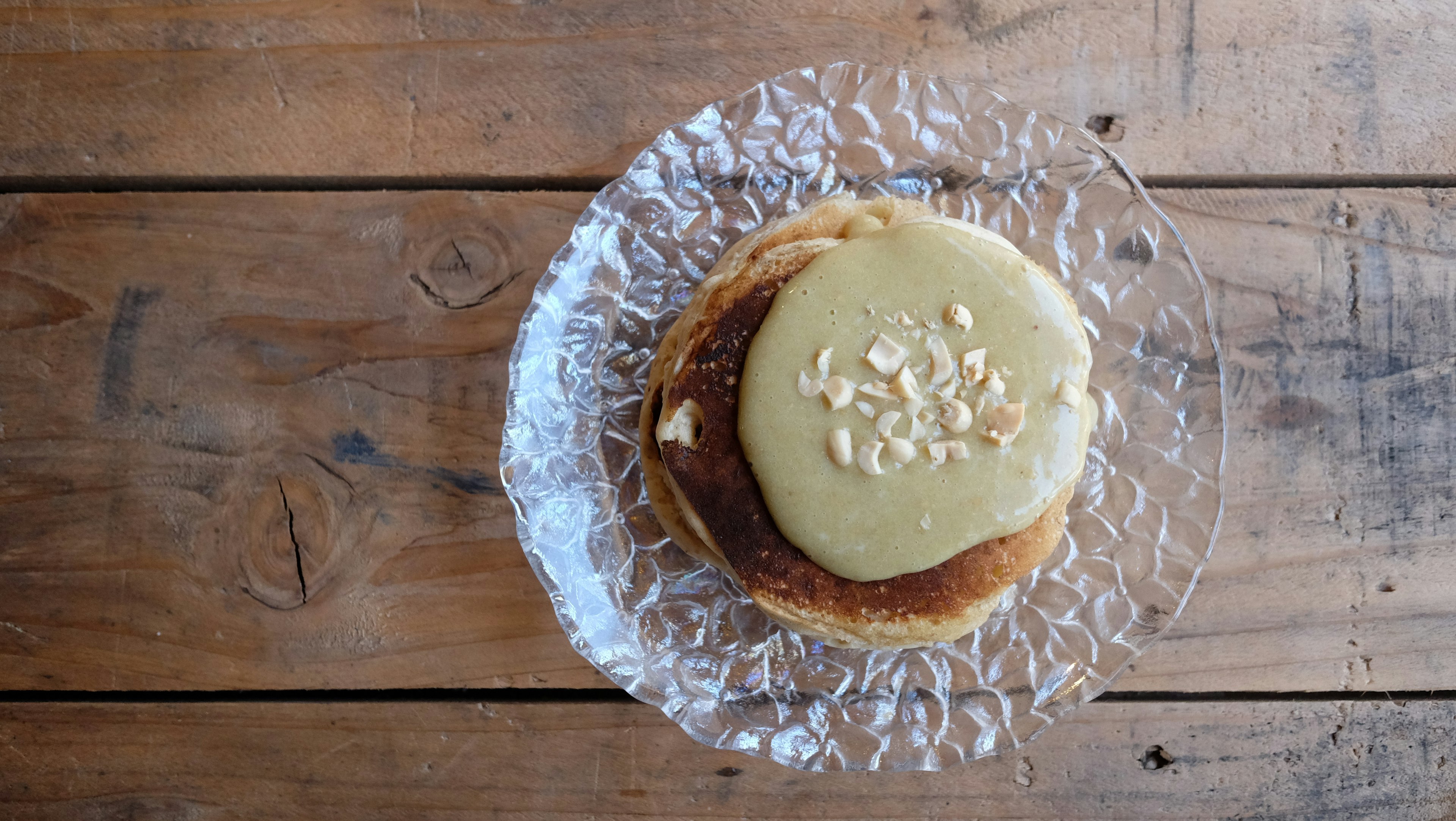 Pancake topped with cream and nuts on a glass plate on a wooden table