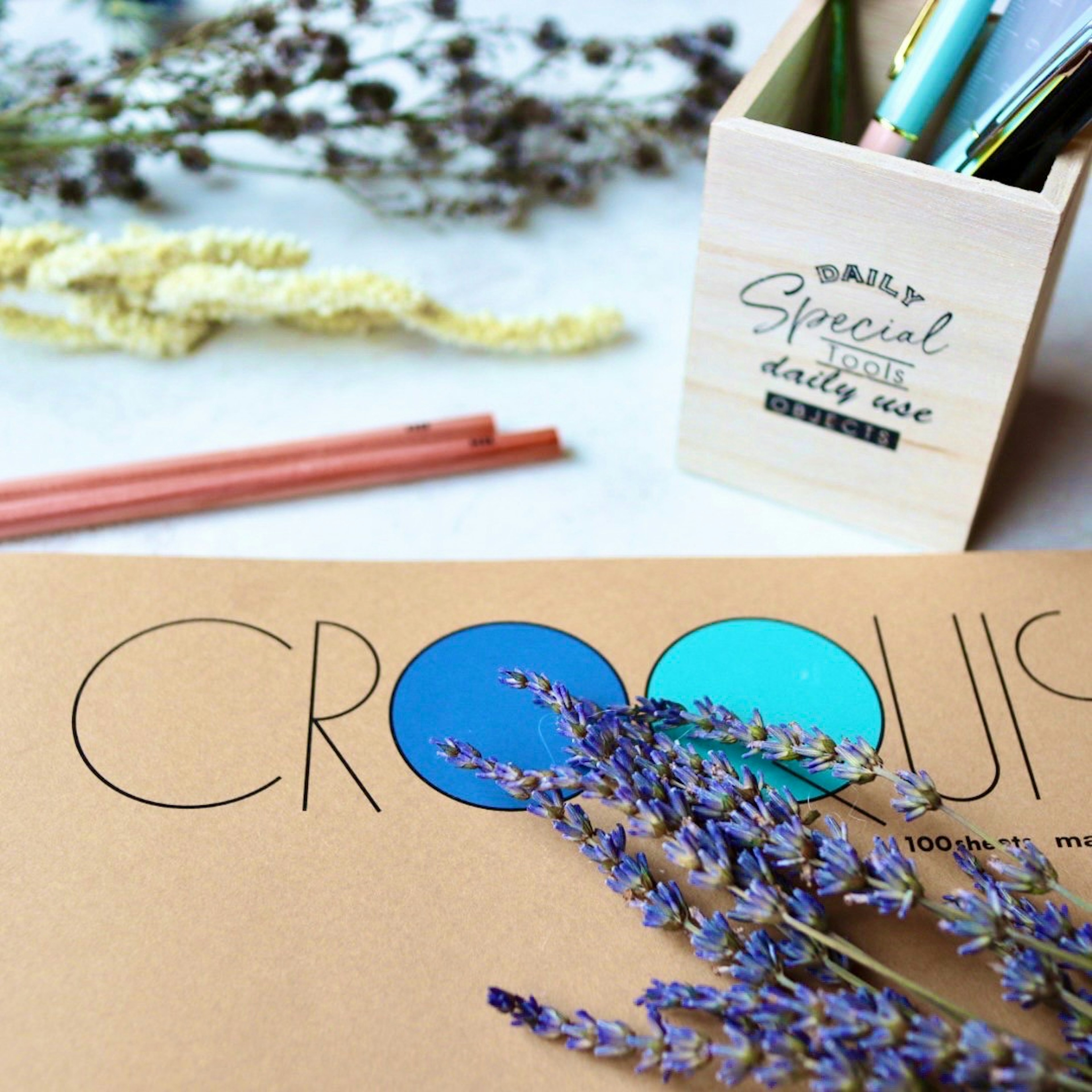 Colorful stationery and dried flowers on a desk with a sketchbook